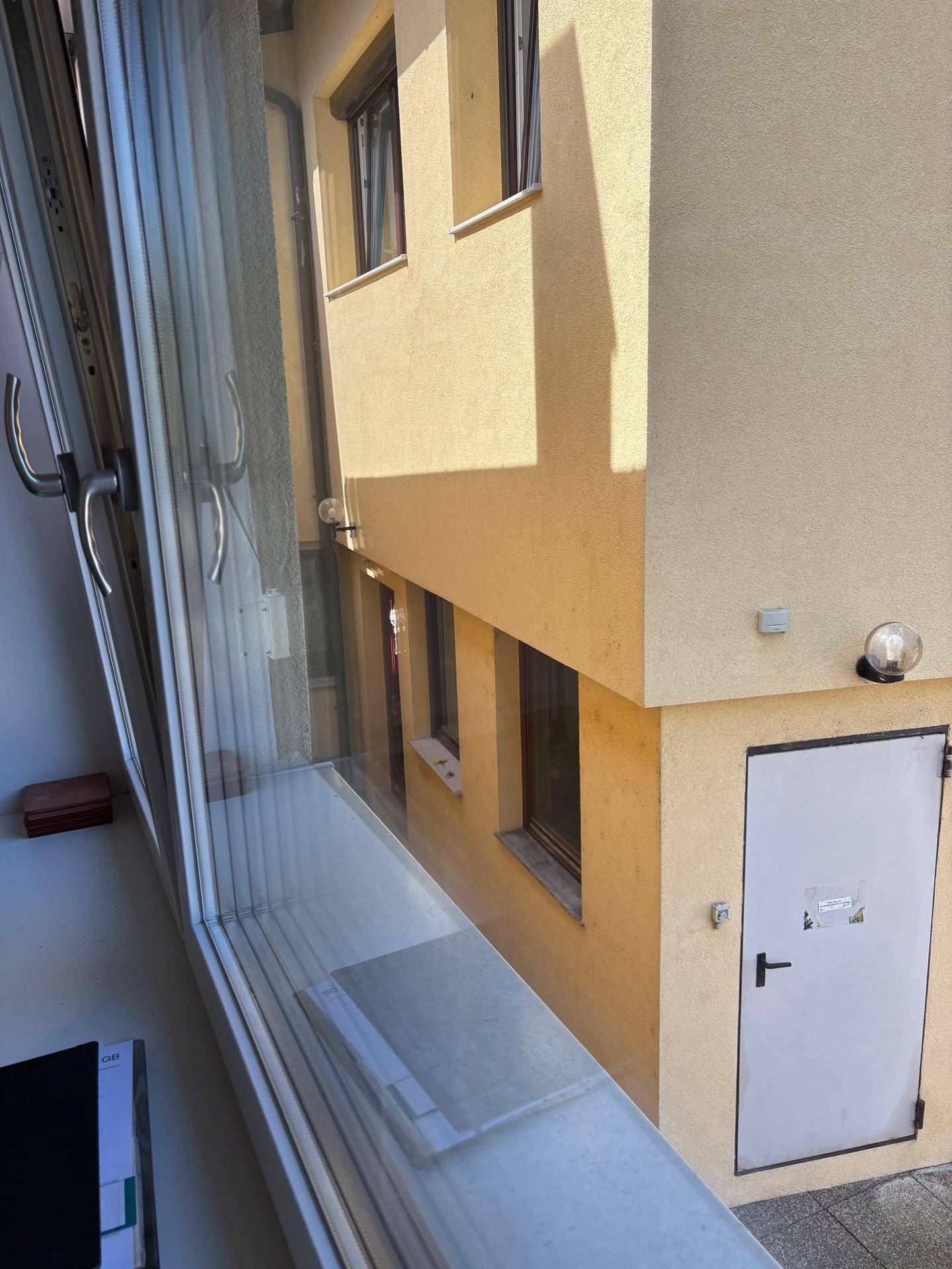 Blick aus einem Fenster auf einen gepflasterten Bereich zwischen gelben Gebäuden.