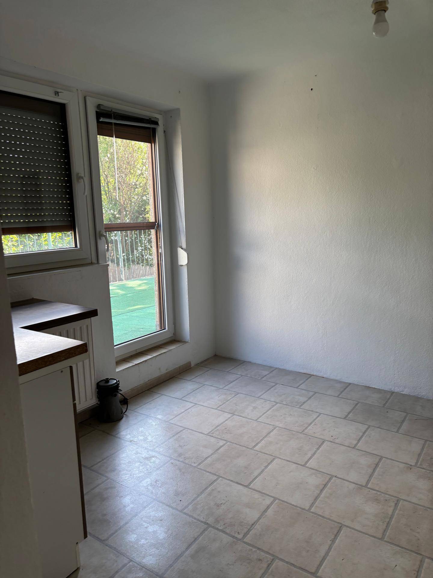 Helle Küche mit Fliesenboden, einem Fenster mit Rollladen und Zugang zu einem Außenbereich.