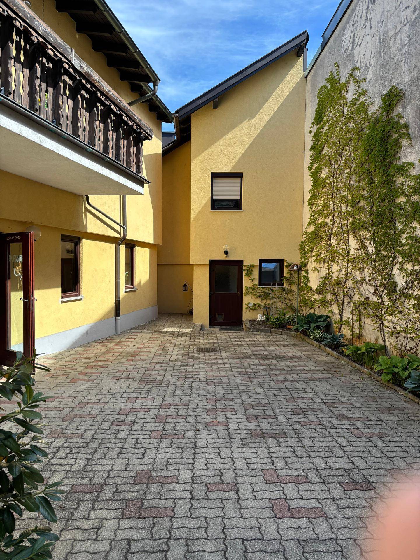 Ein gepflasterter Innenhof zwischen zwei gelben Gebäuden mit einer Kletterpflanze an der Wand.