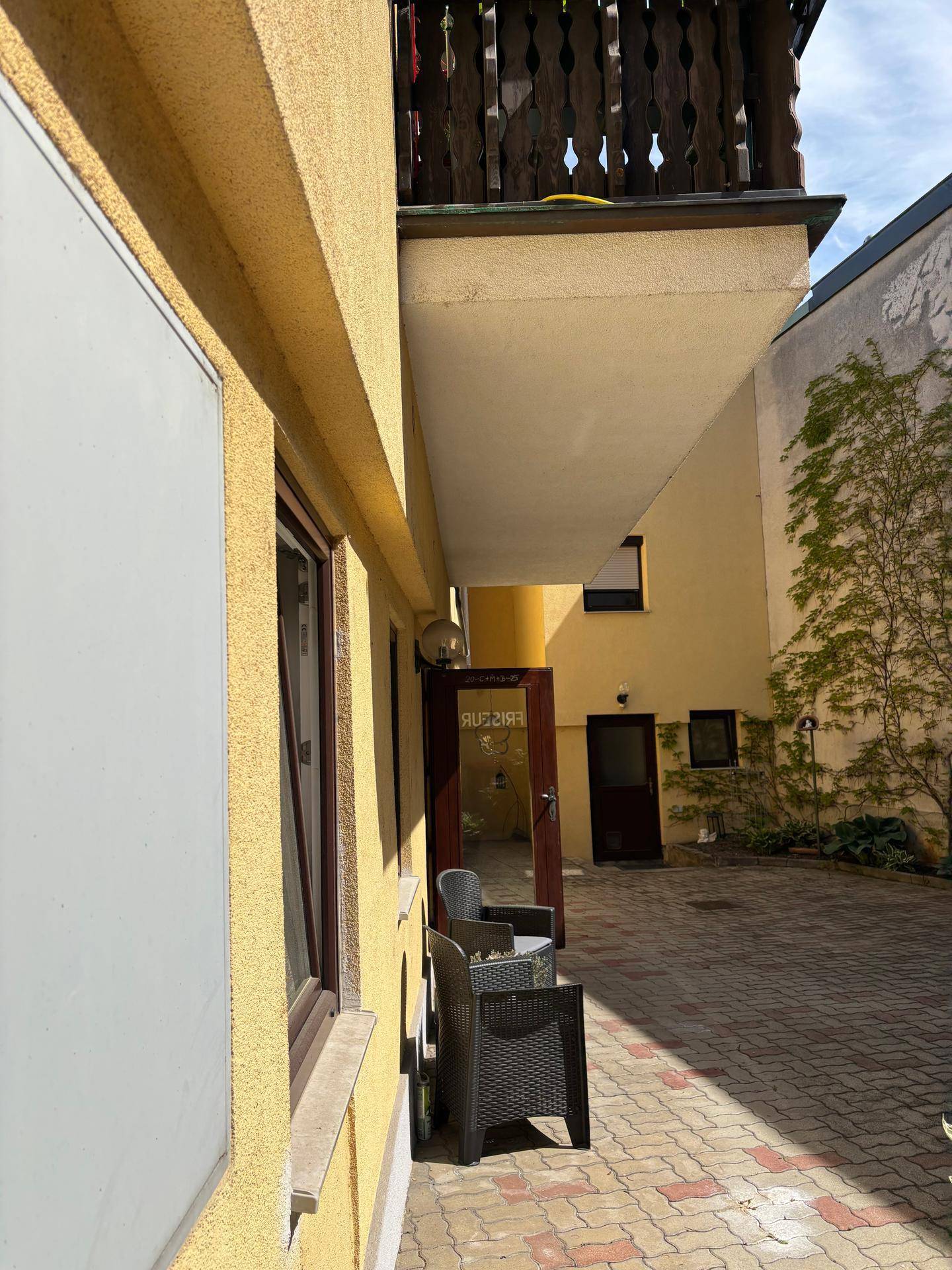 Ein sonniger Innenhof mit Sitzgelegenheiten und einem traditionellen Holzbalkon am gelben Gebäude.