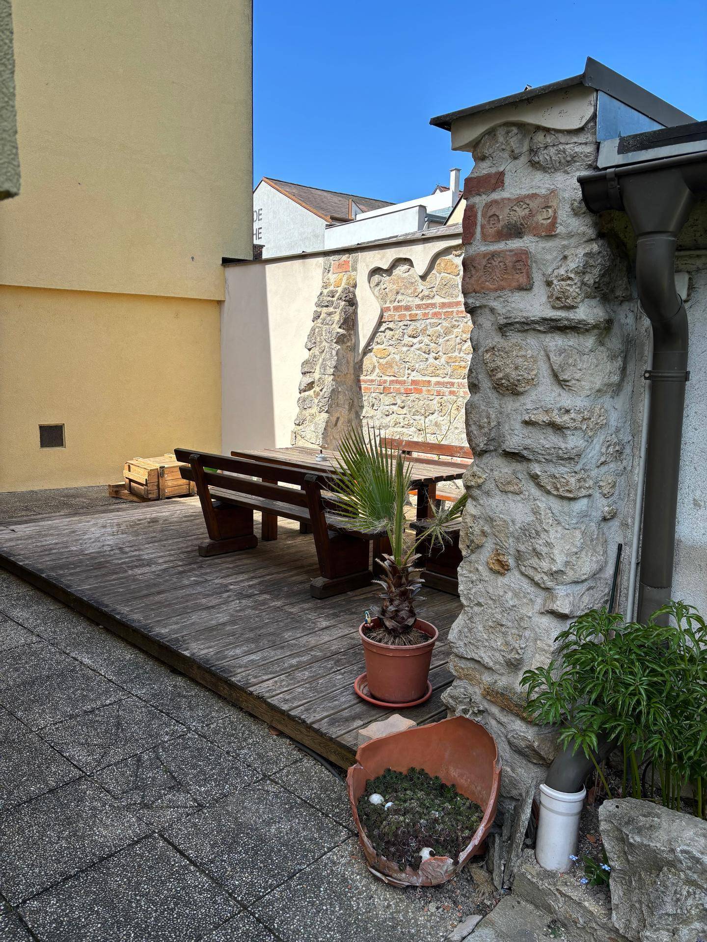 Eine Holzterrasse mit Sitzgelegenheiten und einer Steinmauer, umgeben von Pflanzen.