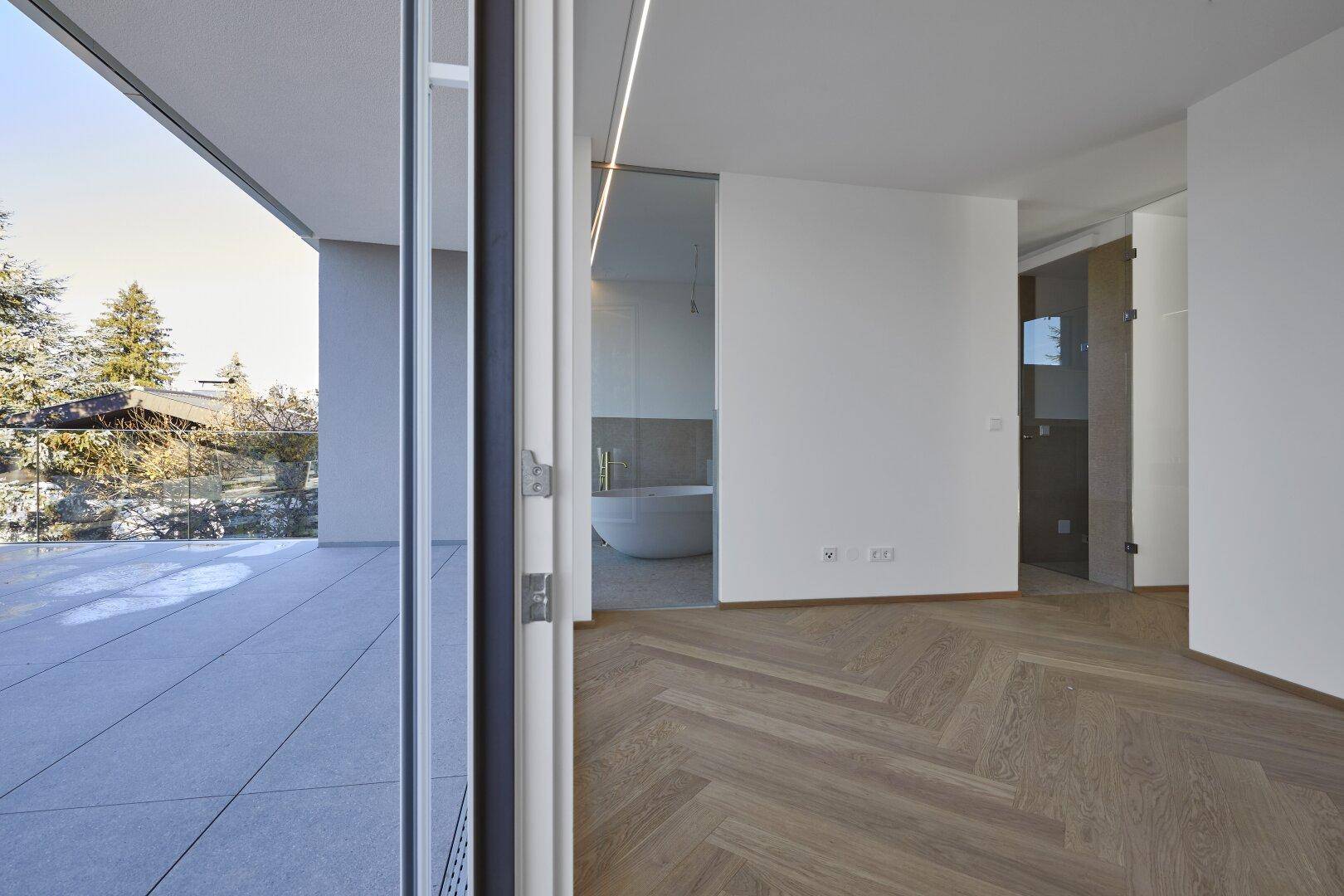 Schlafzimmer mit Fischgrätparkett und direktem Zugang zu einer modernen Terrasse und Badezimmer.