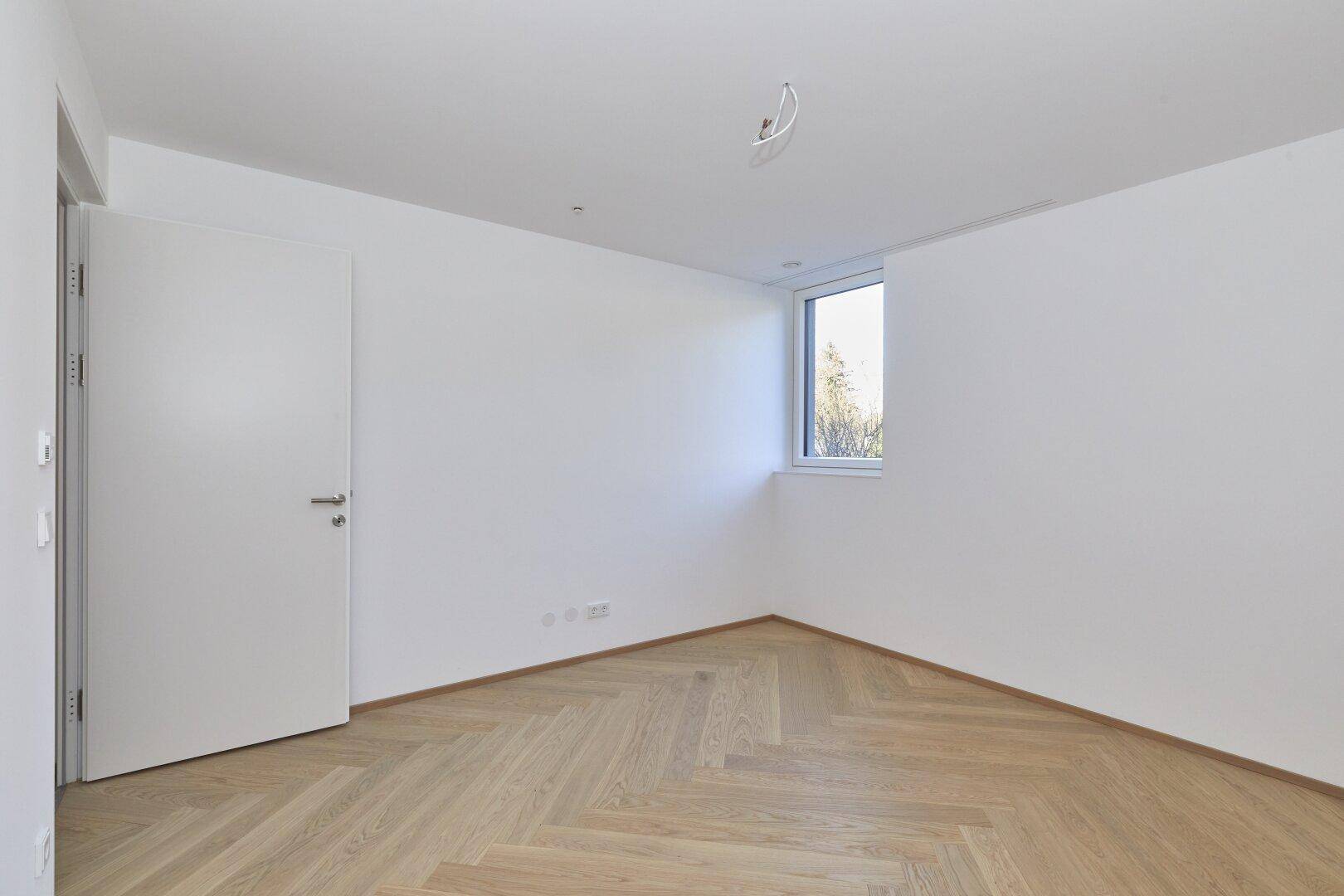 Helles Schlafzimmer mit Fischgrätparkett und einem Fenster, bereit zur individuellen Gestaltung.
