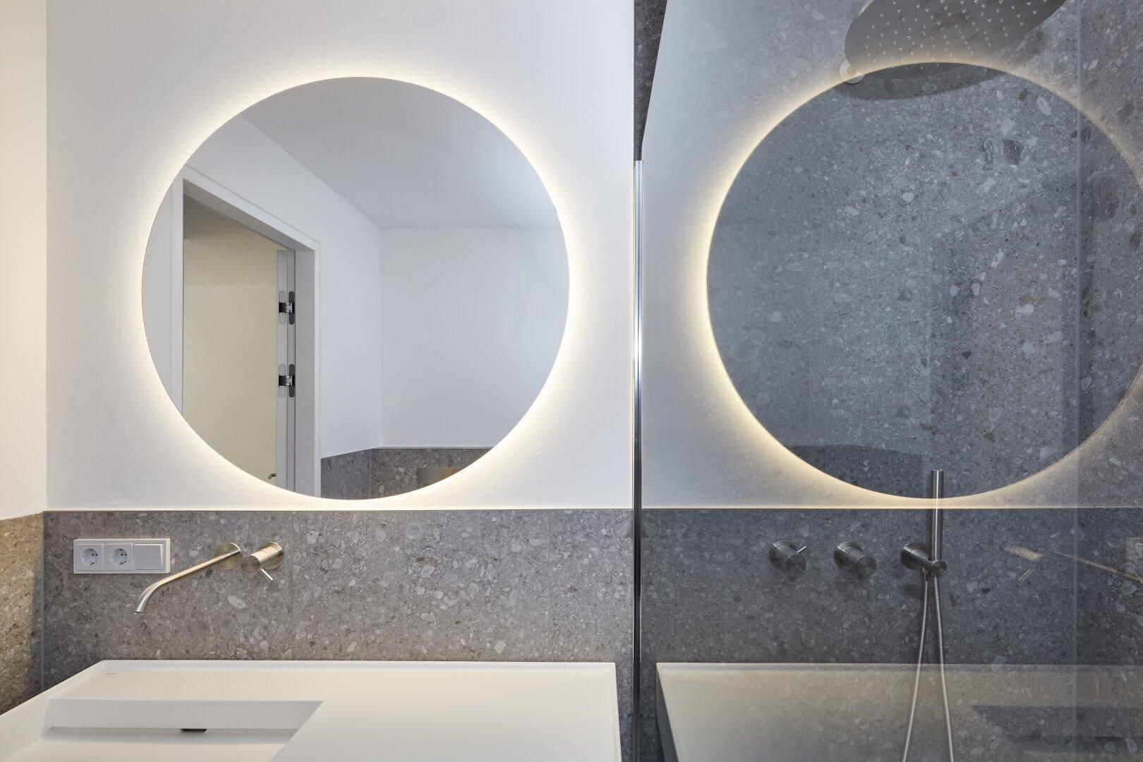 Modernes Badezimmer mit beleuchtetem Spiegel, Einzelwaschbecken und begehbarer Dusche.