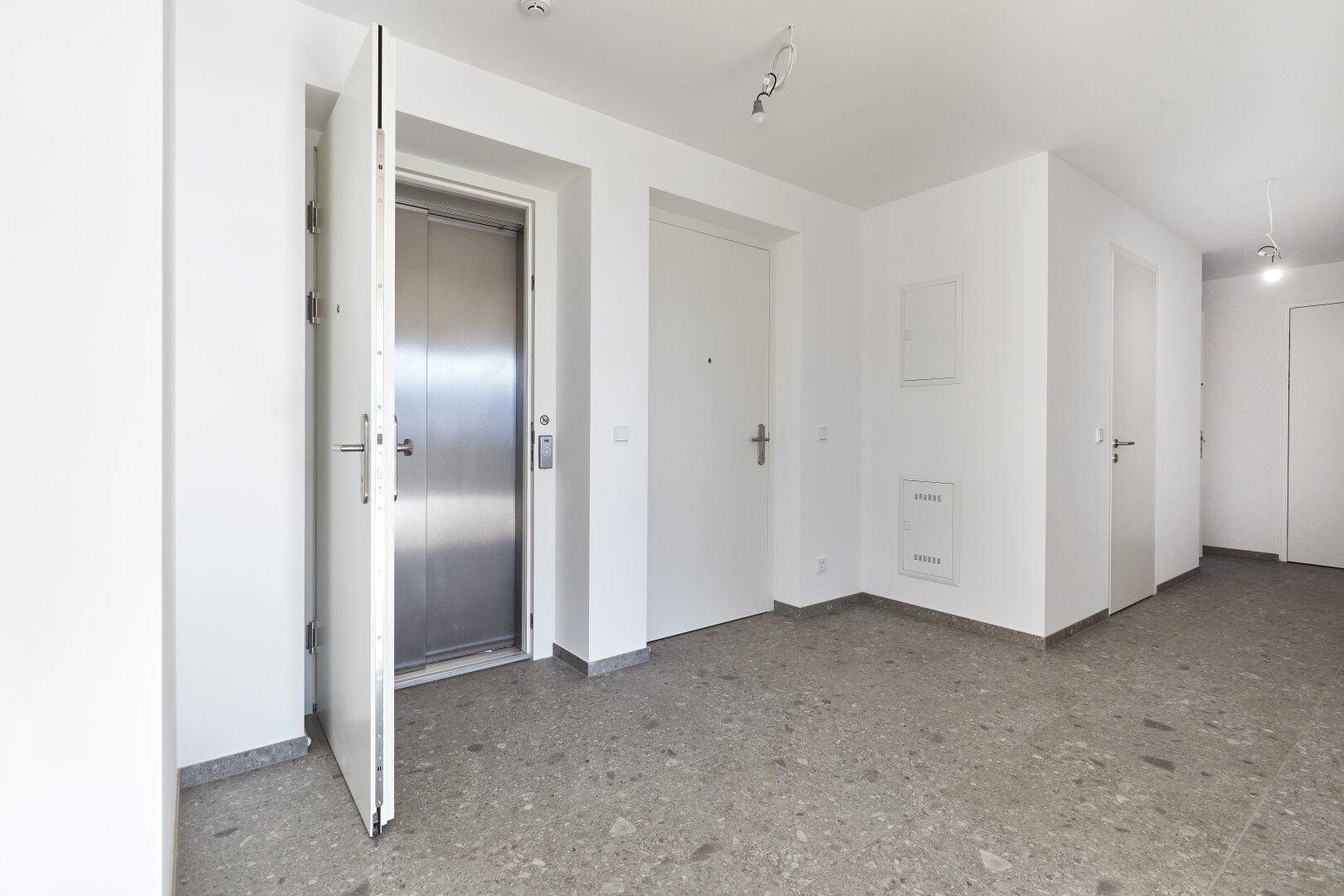 Heller Eingangsbereich mit Aufzug und Fliesenboden in einem modernen Gebäude.