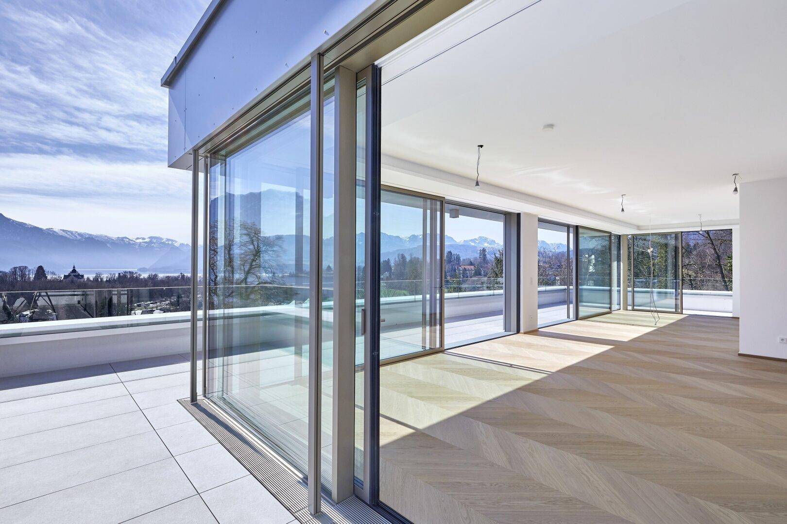 Weitläufiger Wohnraum mit Fischgrätparkett und durchgehender Fensterfront zur Terrasse.