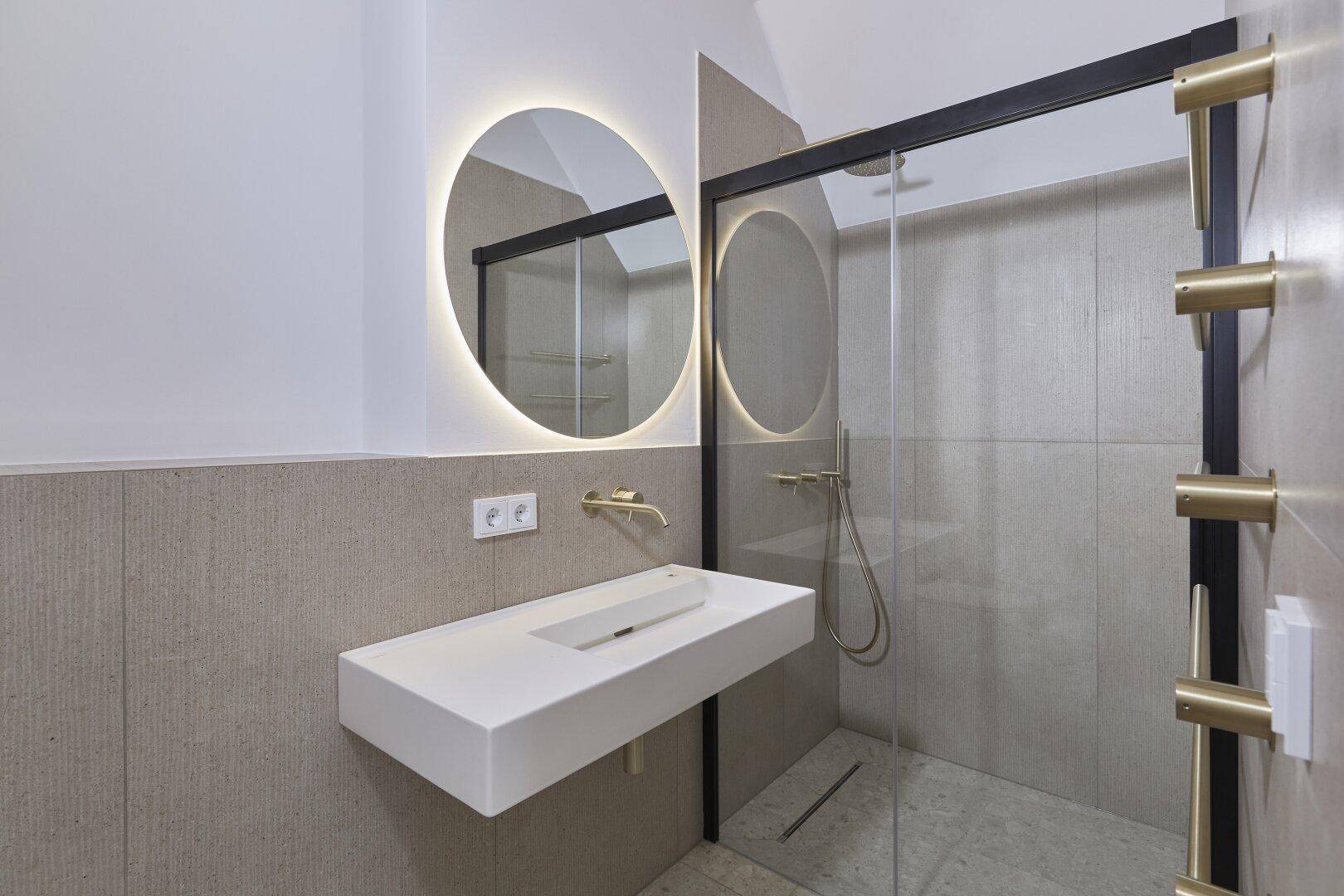 Modernes Badezimmer mit schwebendem Waschtisch, beleuchtetem Spiegel und begehbarer Dusche.