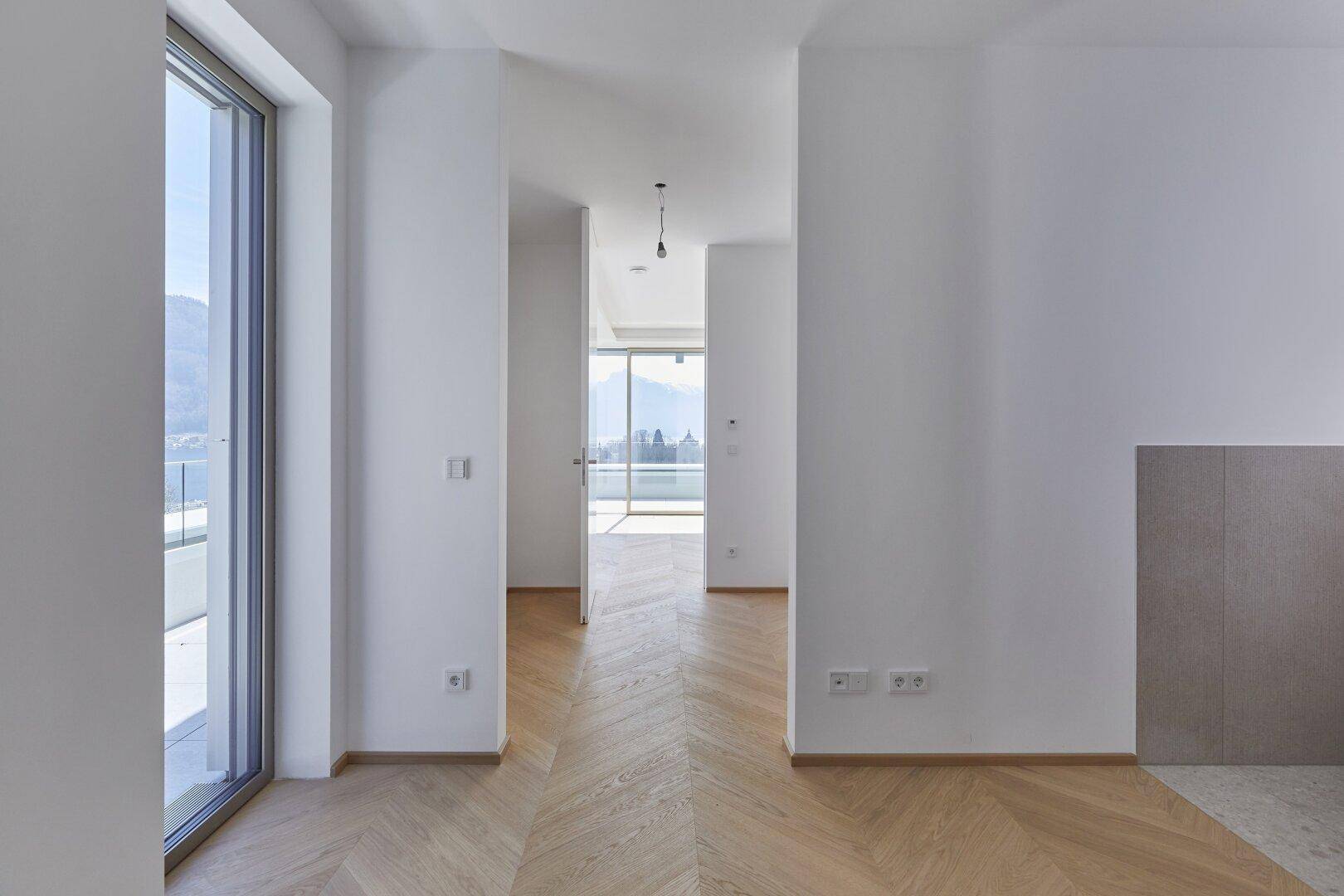 Heller Flur mit Fischgrätparkett, weißen Wänden und Blick in den Wohnbereich.
