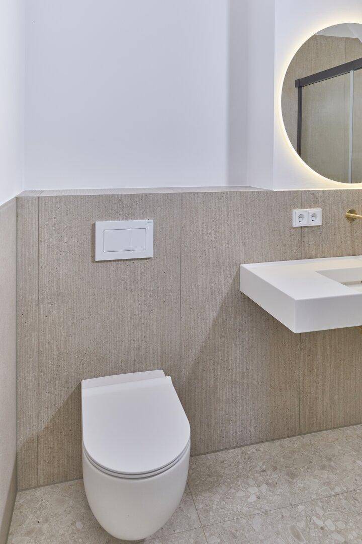 Modernes WC mit wandhängender Toilette, schwebendem Waschtisch und beleuchtetem Spiegel.