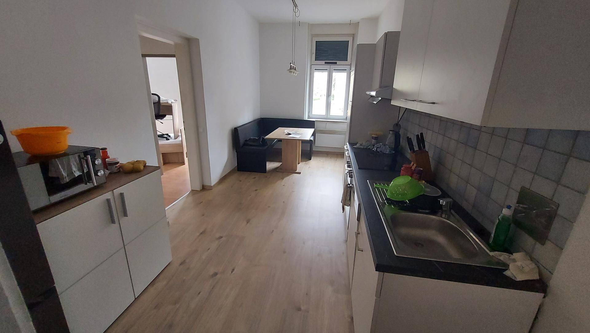 Offene Küche mit Essbereich und hellem Laminatboden, führt zu einem weiteren Raum.