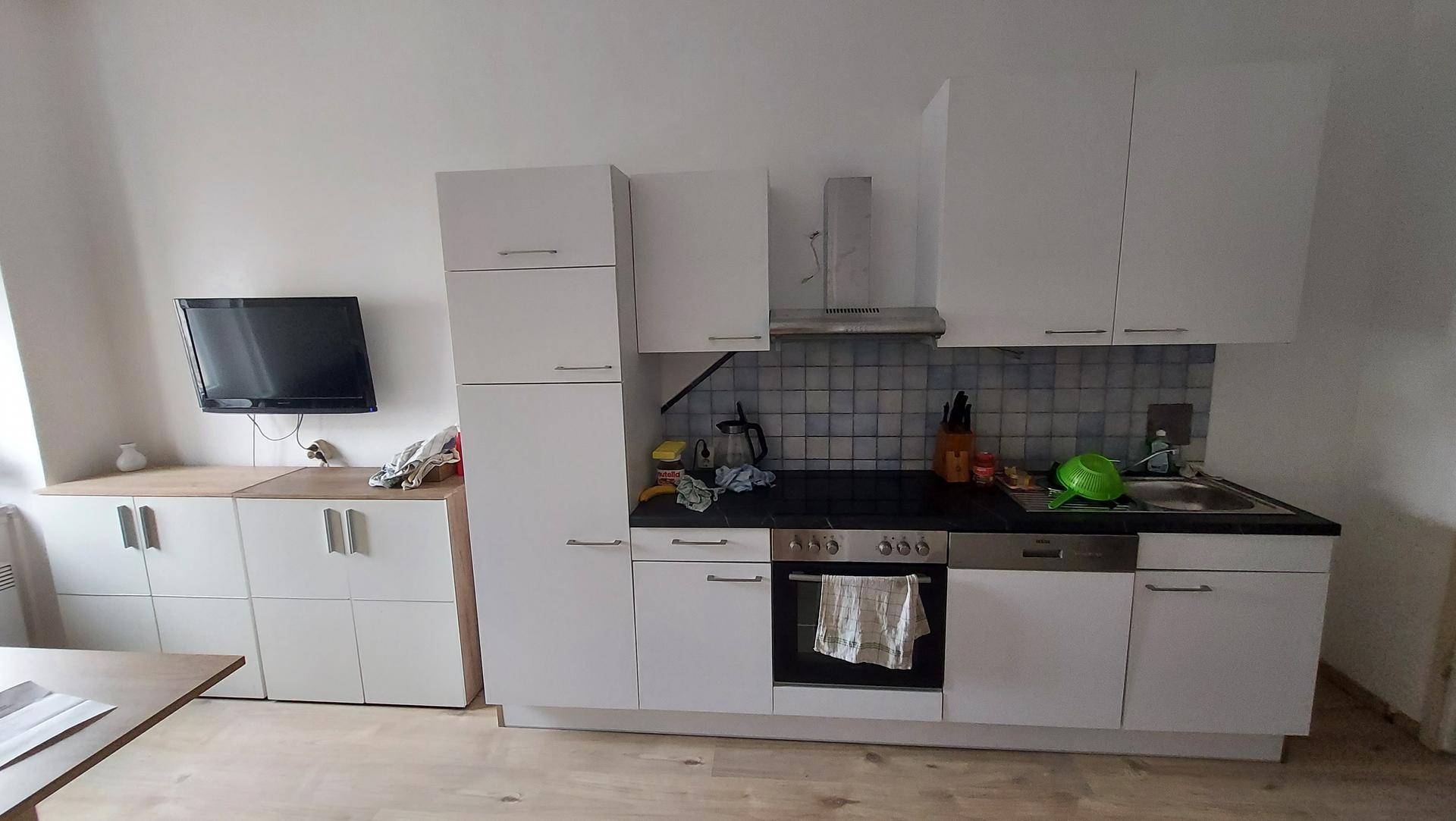 Küchenbereich mit Einbaugeräten, Spüle, Kochfeld und einem an der Wand montierten Fernseher.