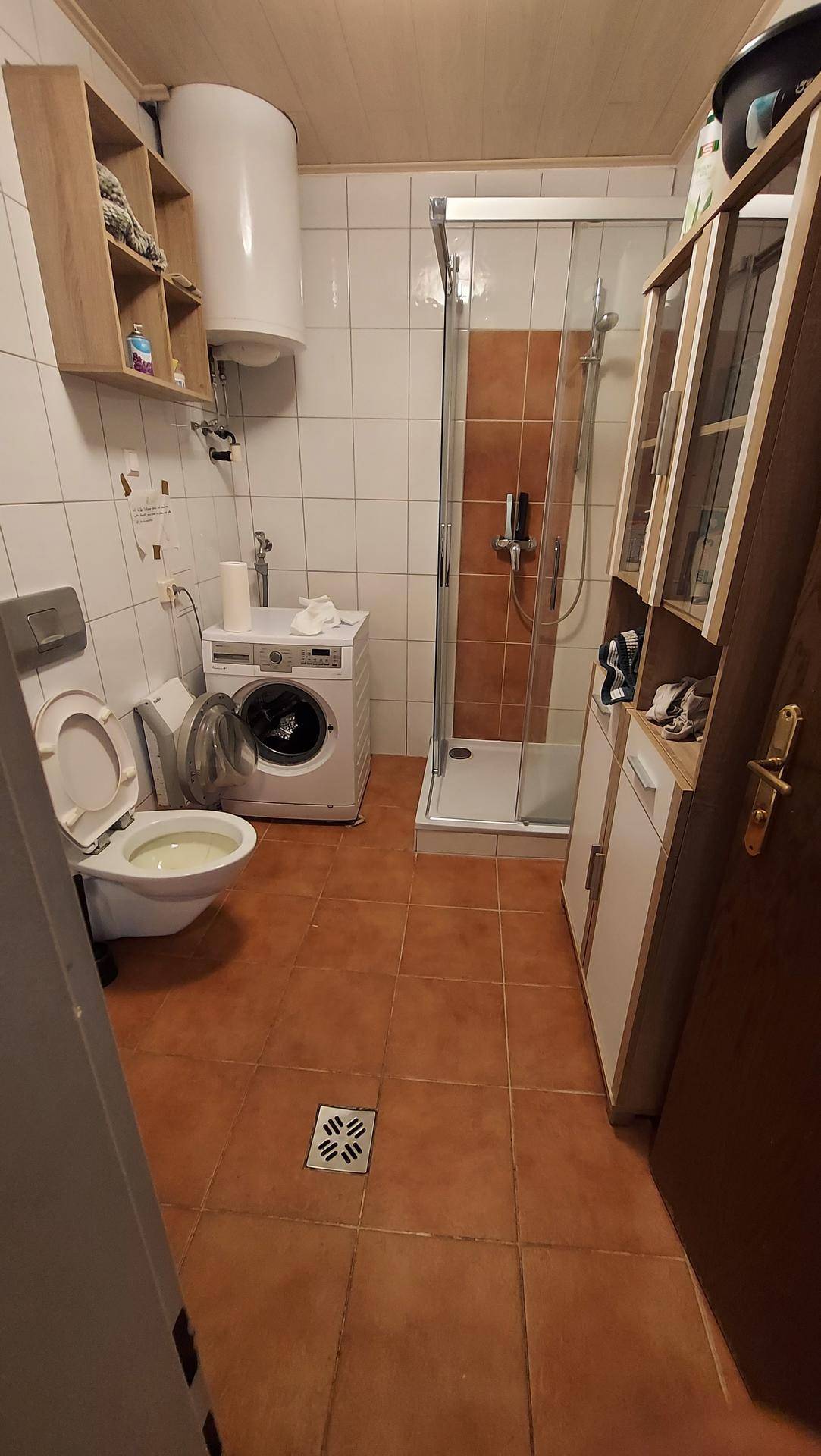 Funktionales Badezimmer mit Toilette, Waschmaschine, Duschkabine und Warmwasserboiler.