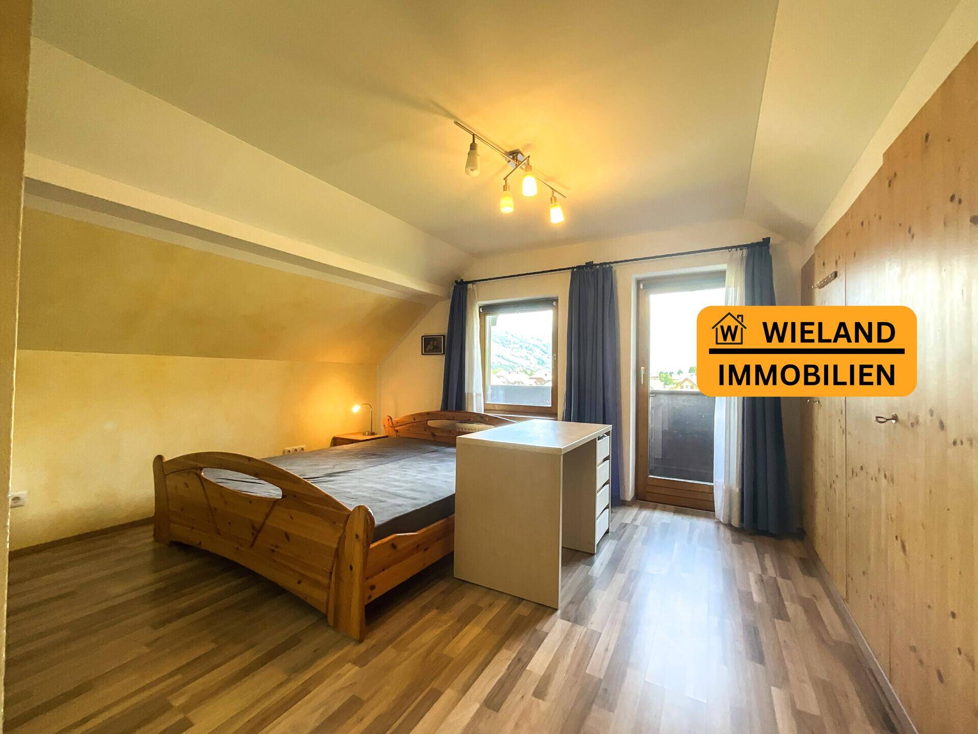 Schlafzimmer mit Holzbett, Schreibtisch, Holzwänden und Balkonzugang.