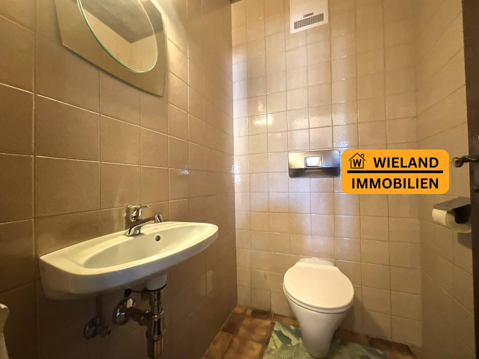 Separate Toilette mit Waschbecken und beigefarbenen Fliesen, funktional und sauber.