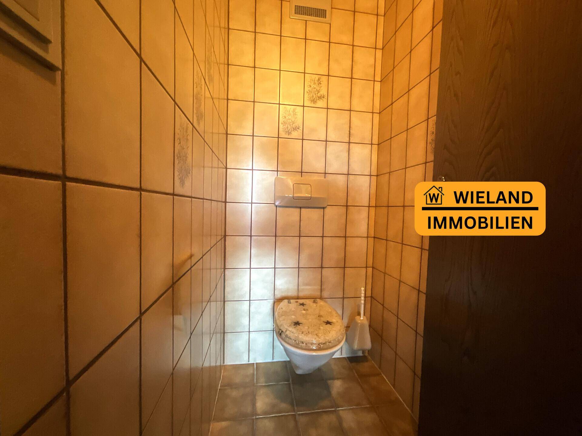 Separate Toilette mit beigefarbenen Fliesen und traditioneller Ausstattung.