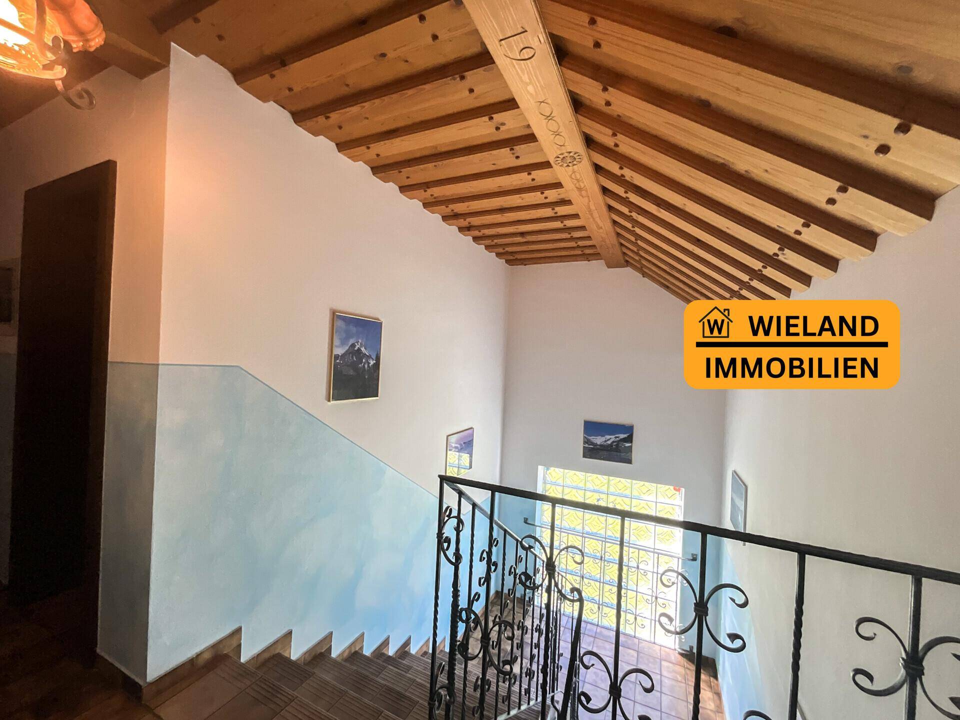 Offenes Treppenhaus mit sichtbaren Holzbalken und schmiedeeisernem Geländer, hell und geräumig.