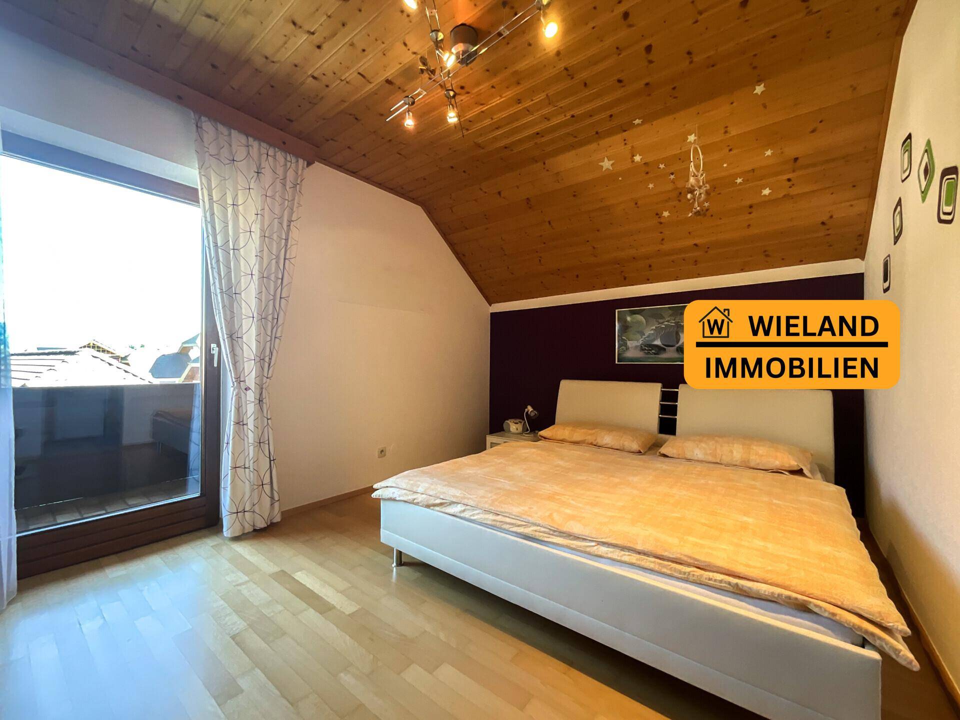 Schlafzimmer mit Holzboden, schräger Holzdecke und Balkonzugang, bietet Bergblick.