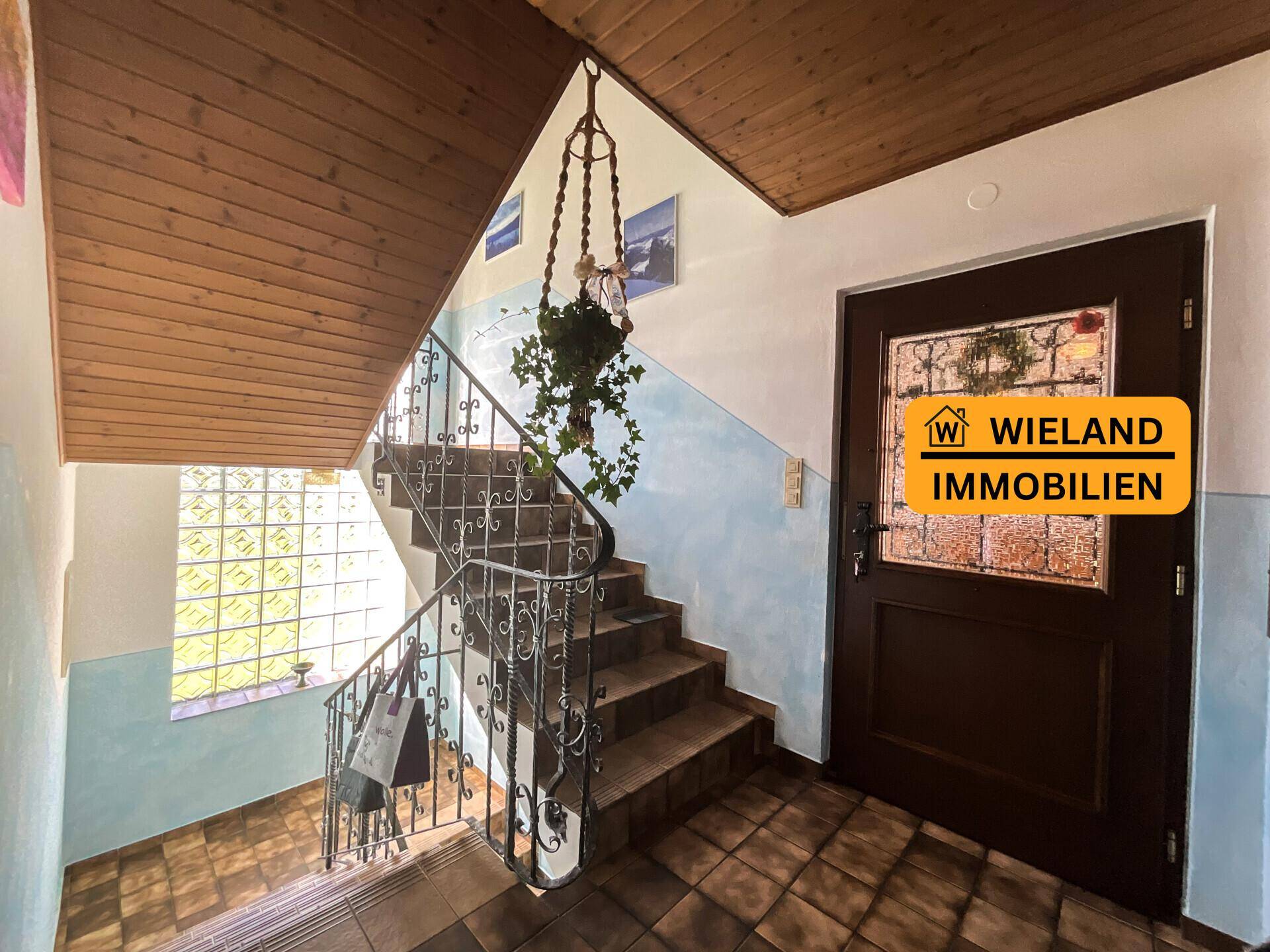 Treppenhaus mit schmiedeeisernem Geländer, Fliesenboden und Holzdecke, führt in die oberen Etagen.
