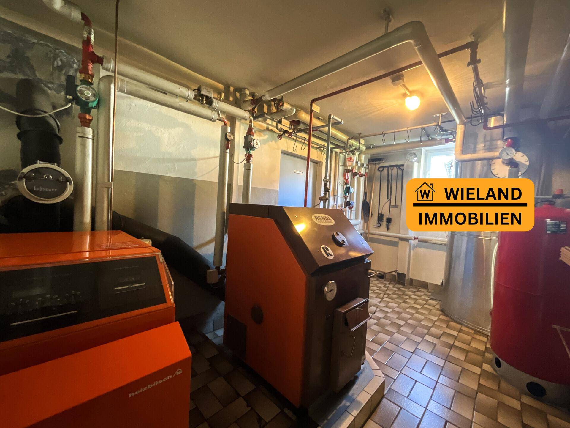 Heizungsraum im Keller mit zwei Heizkesseln und sichtbaren Rohren, funktional eingerichtet.
