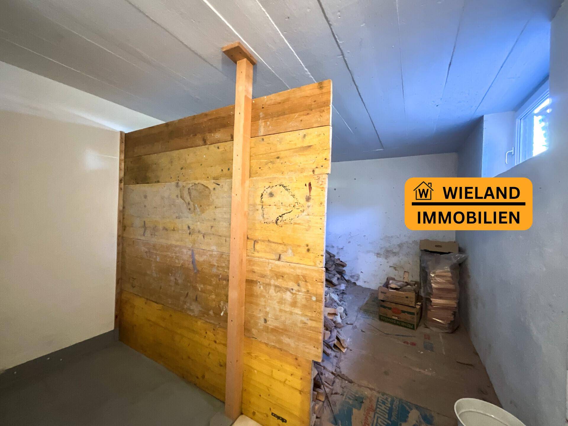 Unausgebauter Kellerraum mit Holzwand und Fenster, bietet Potenzial für Ausbau.