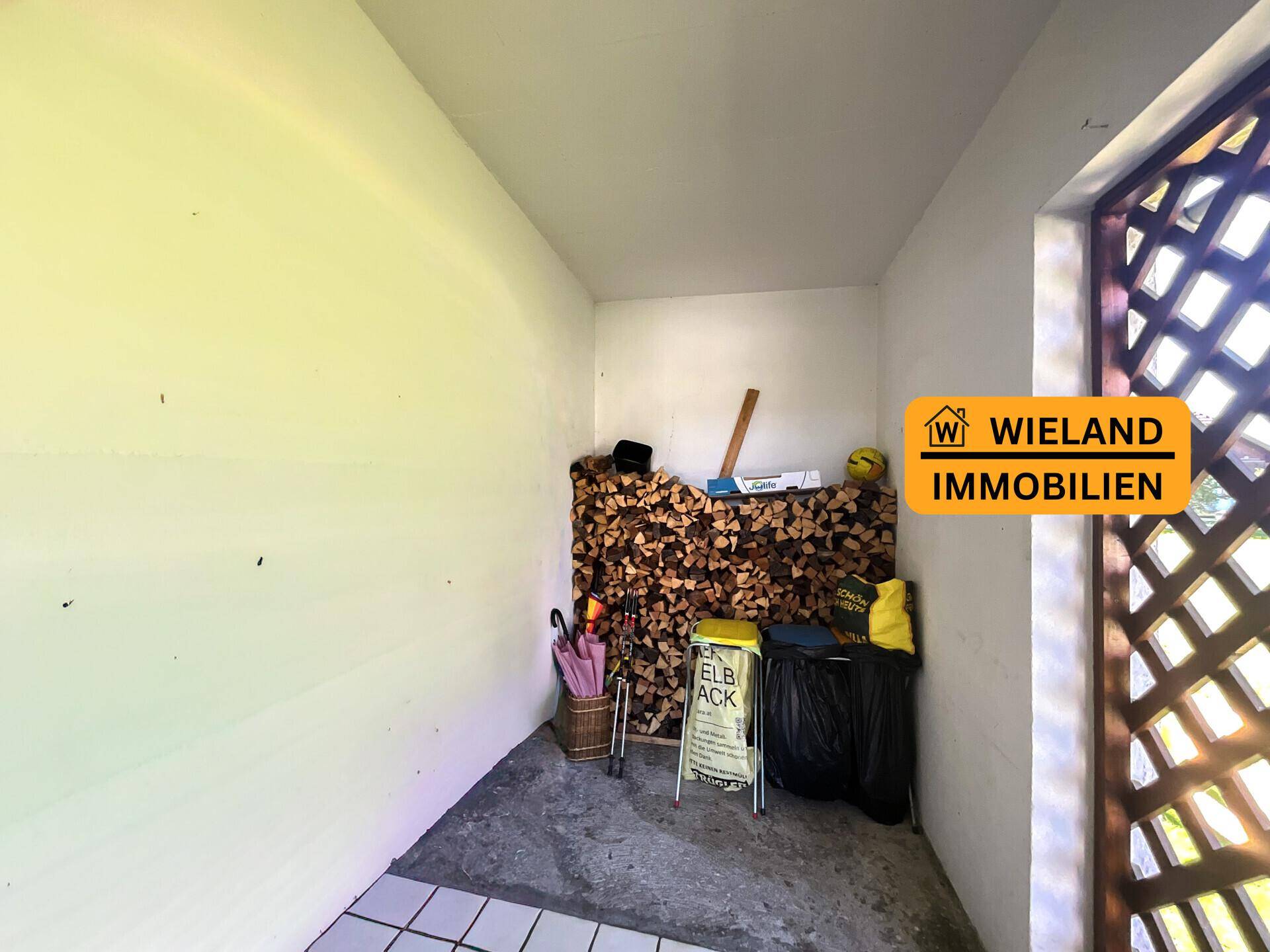 Abstellraum mit Holzstapel und Gitterfenster, ideal für Brennholz und Gartengeräte.