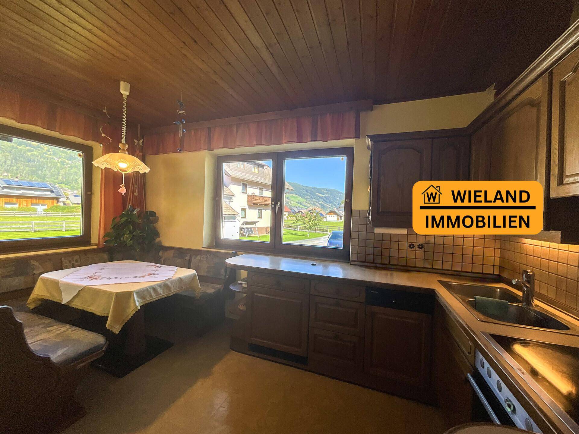 Traditionelle Küche mit Holzeinbauten, Essbereich und Bergblick durch große Fenster.