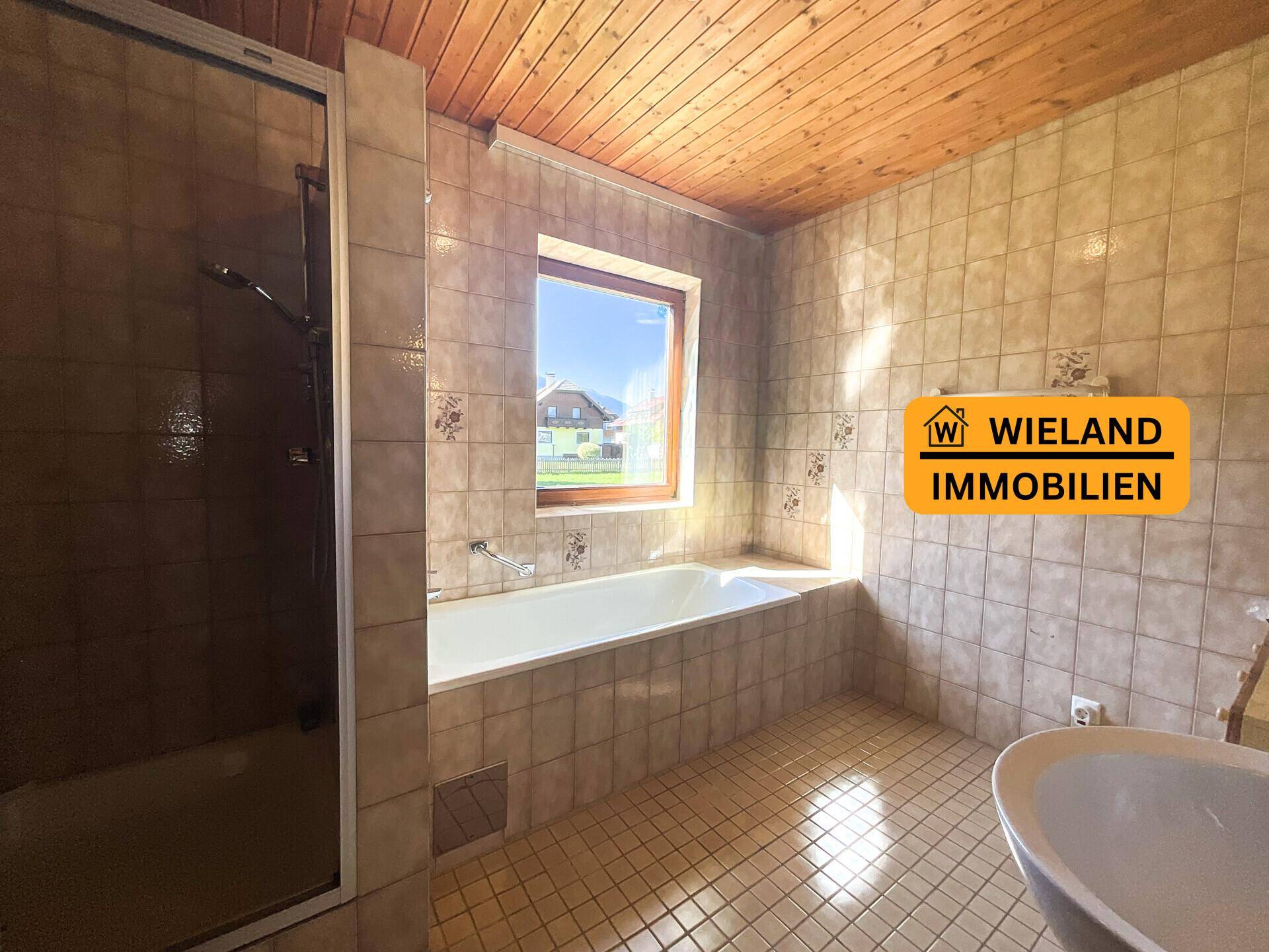 Badezimmer mit beigefarbenen Fliesen, Badewanne und Duschkabine, sowie Holzdecke.