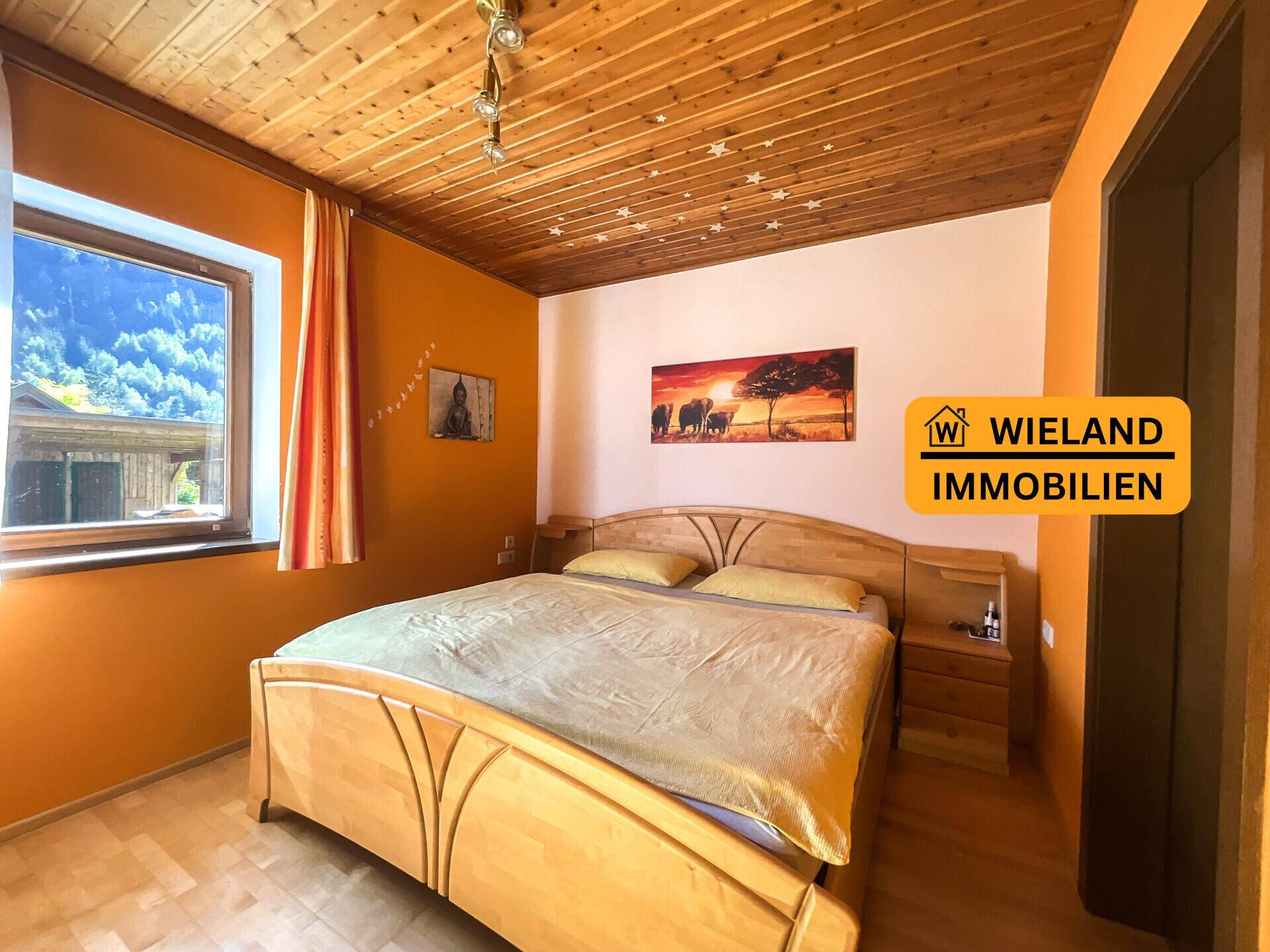 Schlafzimmer mit Holzbett, orangefarbenen Wänden und Holzdecke, mit Blick auf die Berge.
