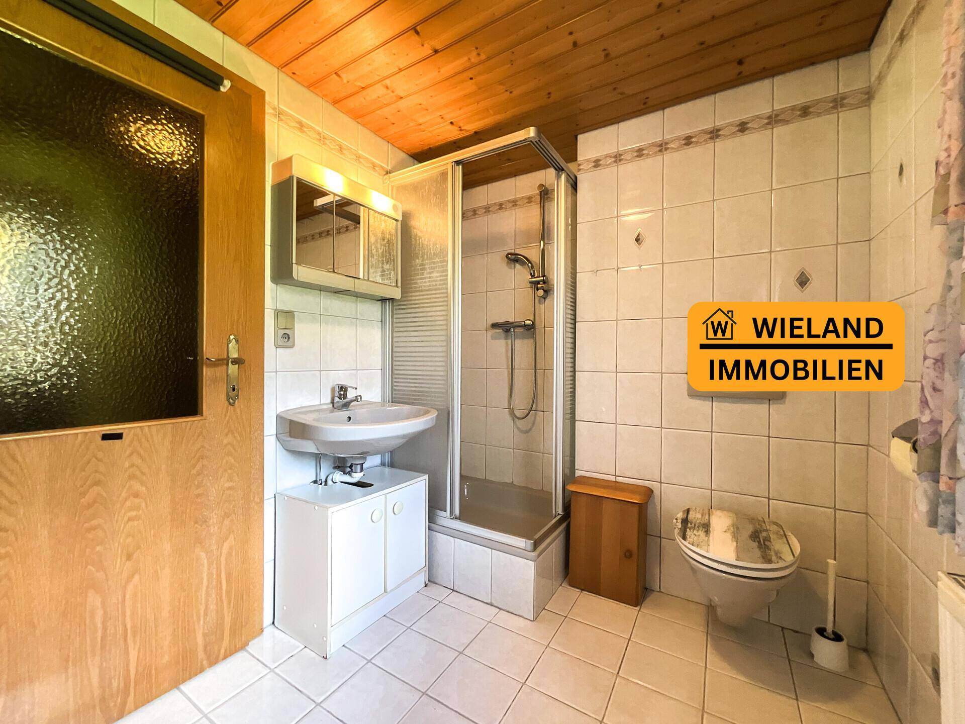 Badezimmer mit Duschkabine, Waschbecken, WC und Holzdecke.