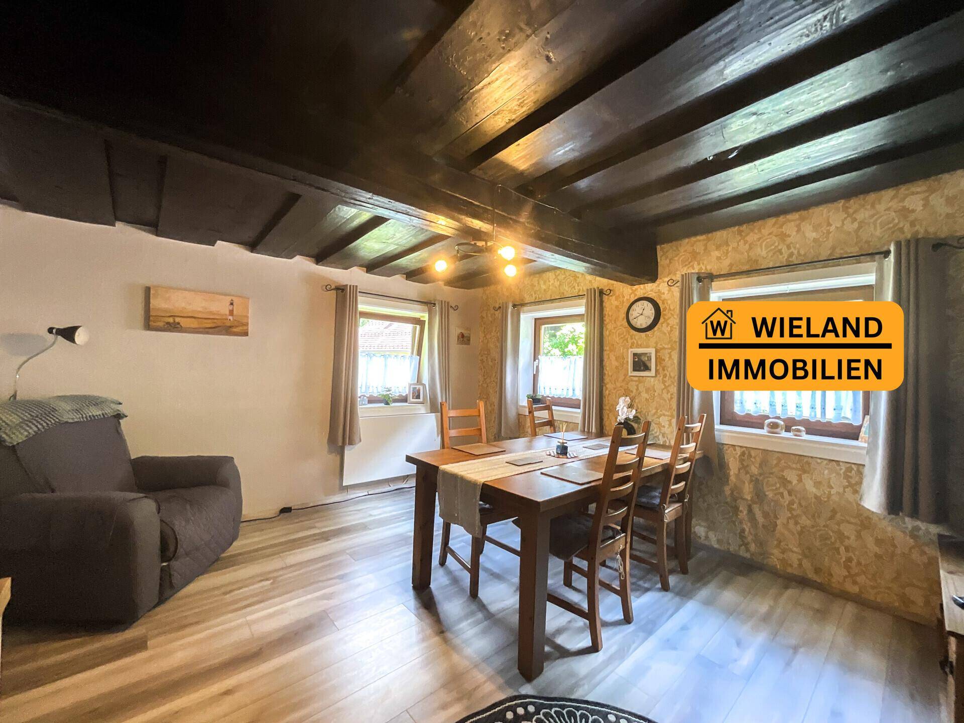 Rustikales Esszimmer mit Holztisch, dunklen Deckenbalken und strukturierten Wänden, ideal für gesellige Runden.
