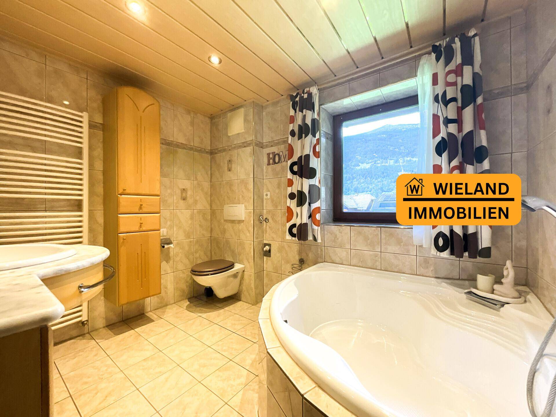 Geräumiges Badezimmer mit Eckbadewanne, WC, Einzelwaschbecken und Fenster mit Ausblick.