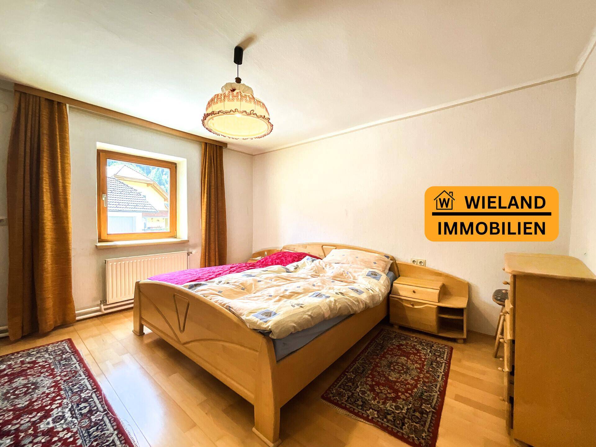 Gemütliches Schlafzimmer mit Holzbett, Nachttischen und Fenster mit Blick nach draußen.
