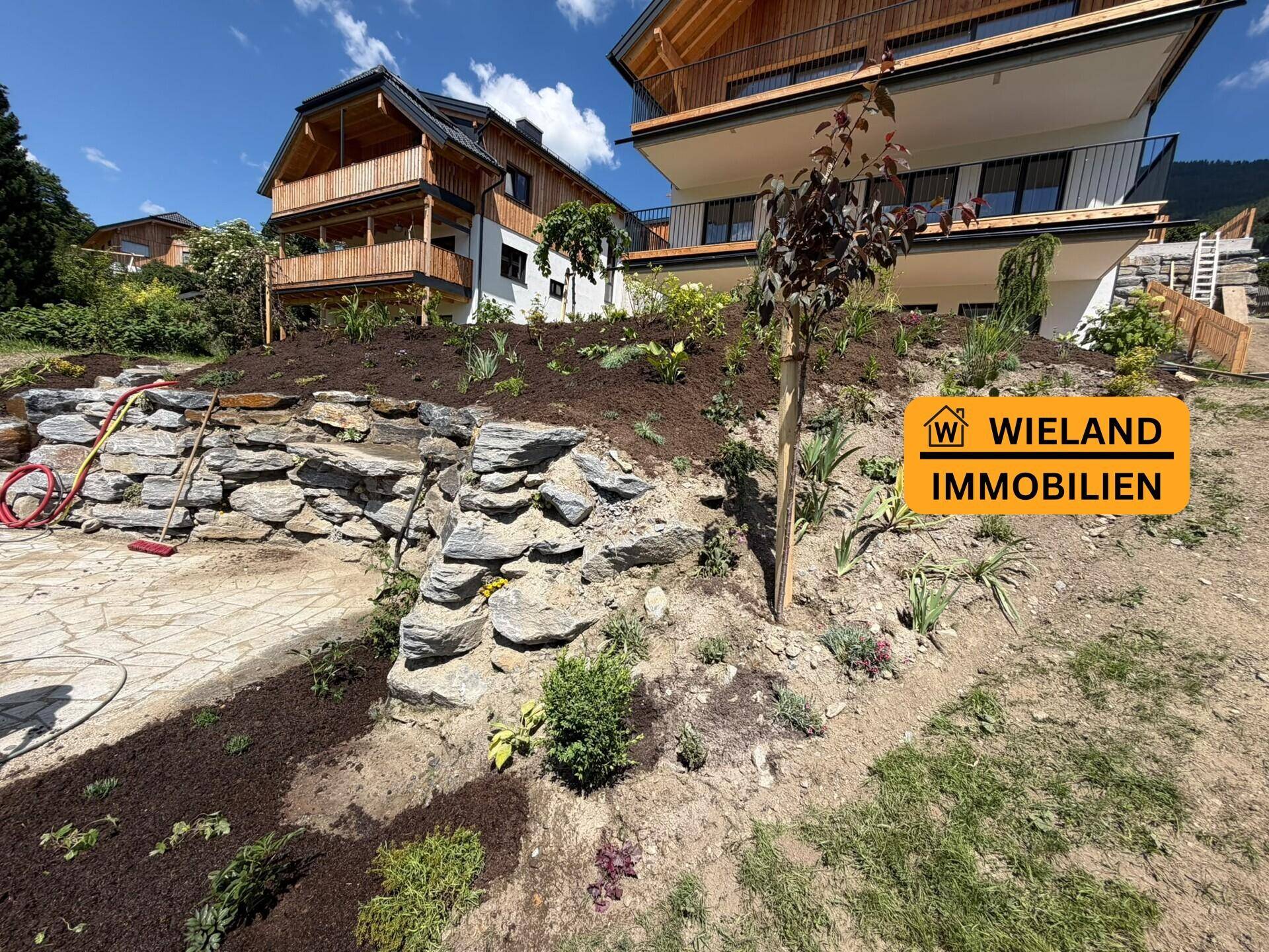 Frisch bepflanzter Garten mit Natursteinmauern und moderner Architektur im Hintergrund.