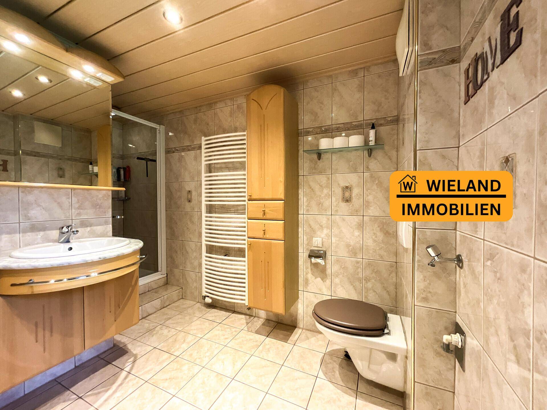Gefliestes Badezimmer mit Dusche, Einzelwaschbecken, WC und beheiztem Handtuchhalter.