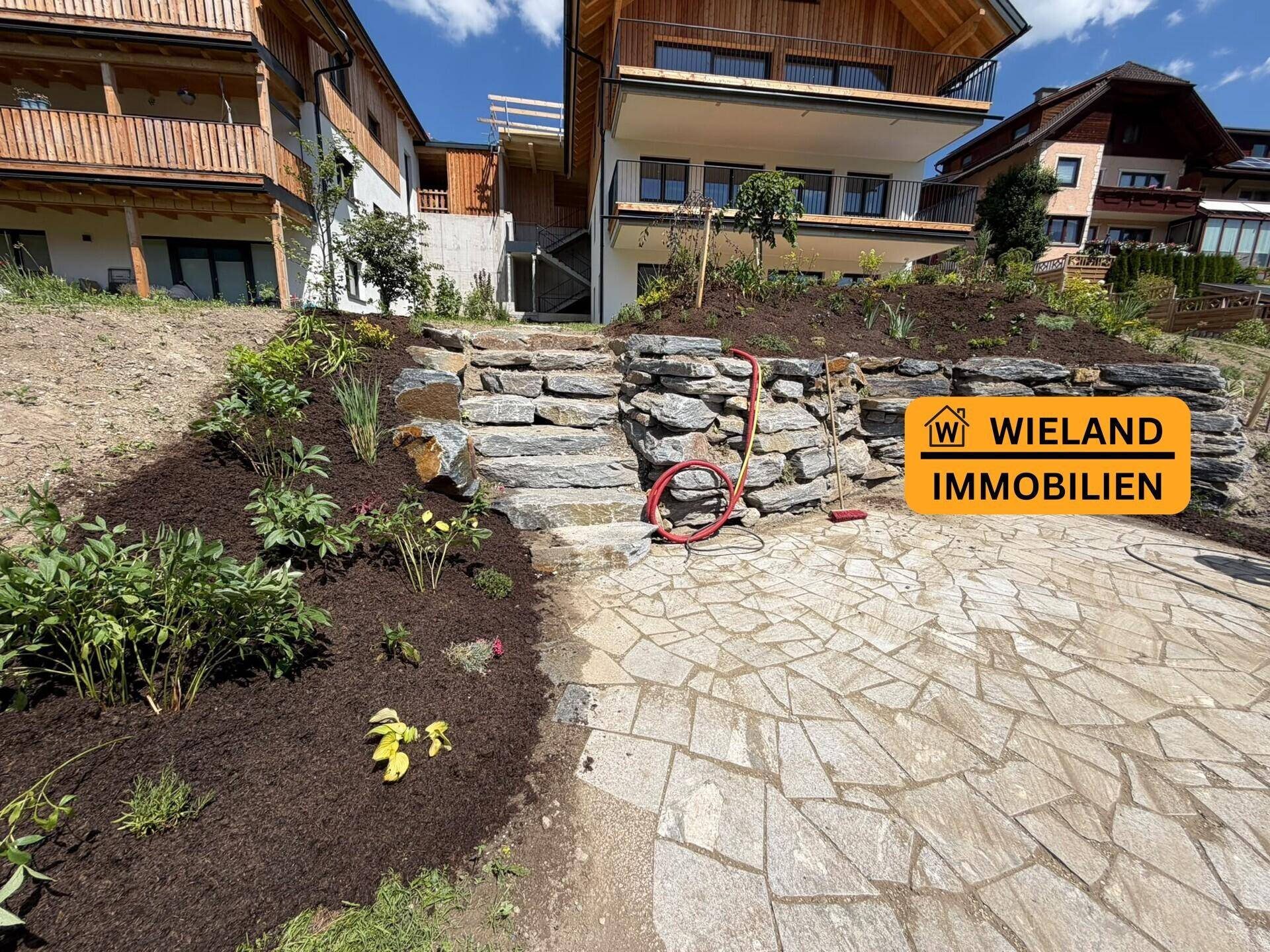 Neu angelegter Gartenbereich mit Natursteintreppe und gepflastertem Weg vor dem Gebäude.