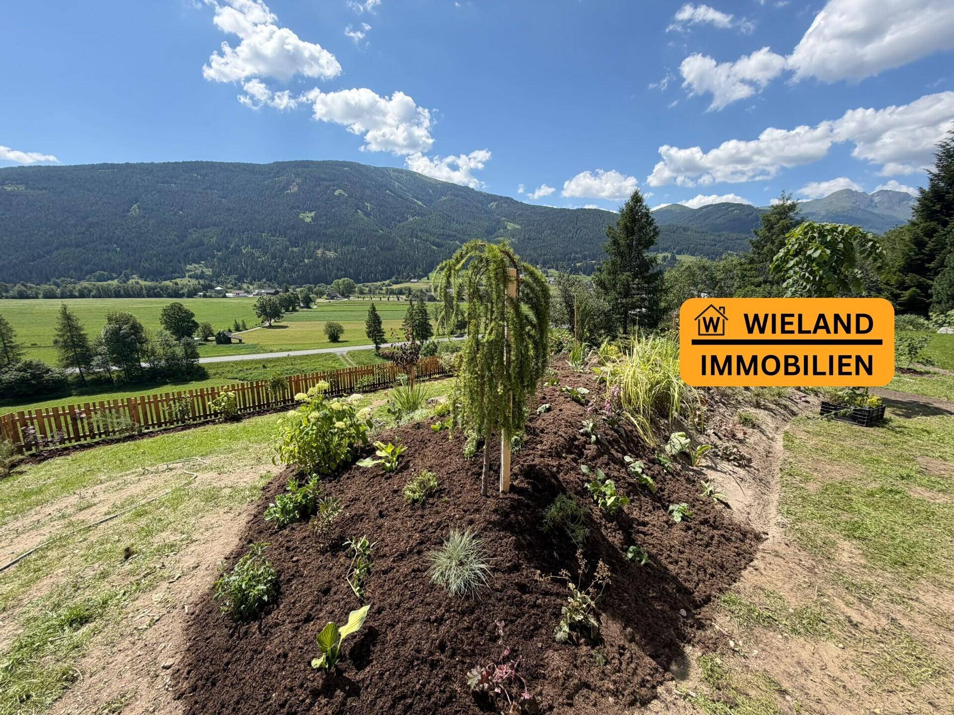 Panoramablick vom neu gestalteten Garten über die weite grüne Landschaft und die Berge.