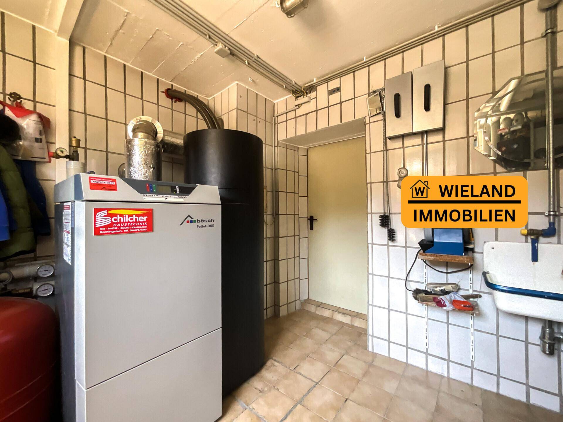 Technikraum mit Heizungsanlage, gefliesten Wänden und kleinem Waschbecken.