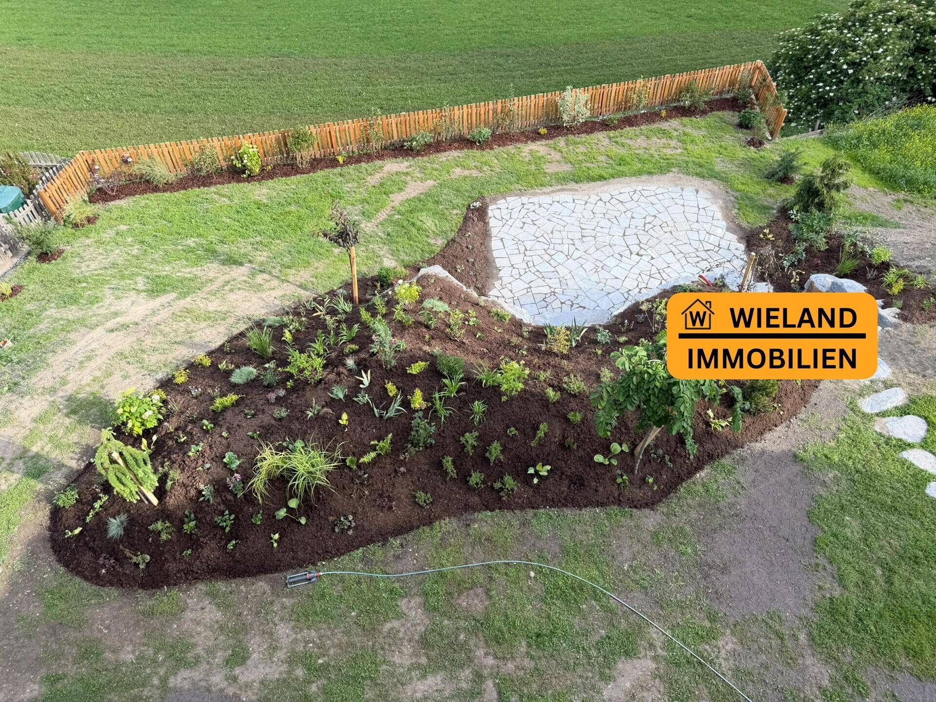 Vogelperspektive des neu gestalteten Gartens mit Rasenfläche und gepflastertem Sitzbereich.