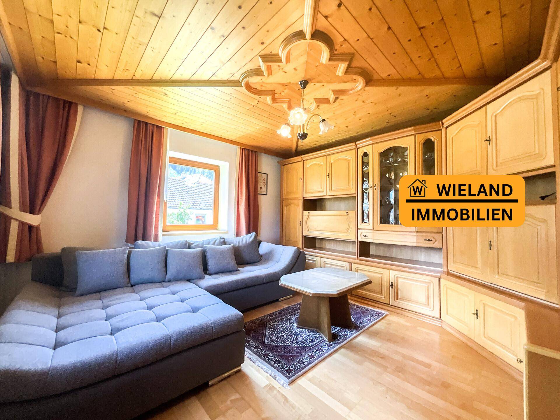Wohnzimmer mit großem Ecksofa, traditioneller Holzschrankwand und Holzboden.
