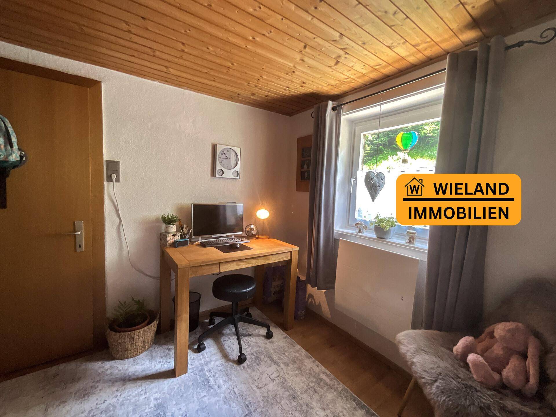 Kleines Arbeitszimmer mit Holzdecke, Schreibtisch und Fenster, das eine angenehme Arbeitsatmosphäre schafft.