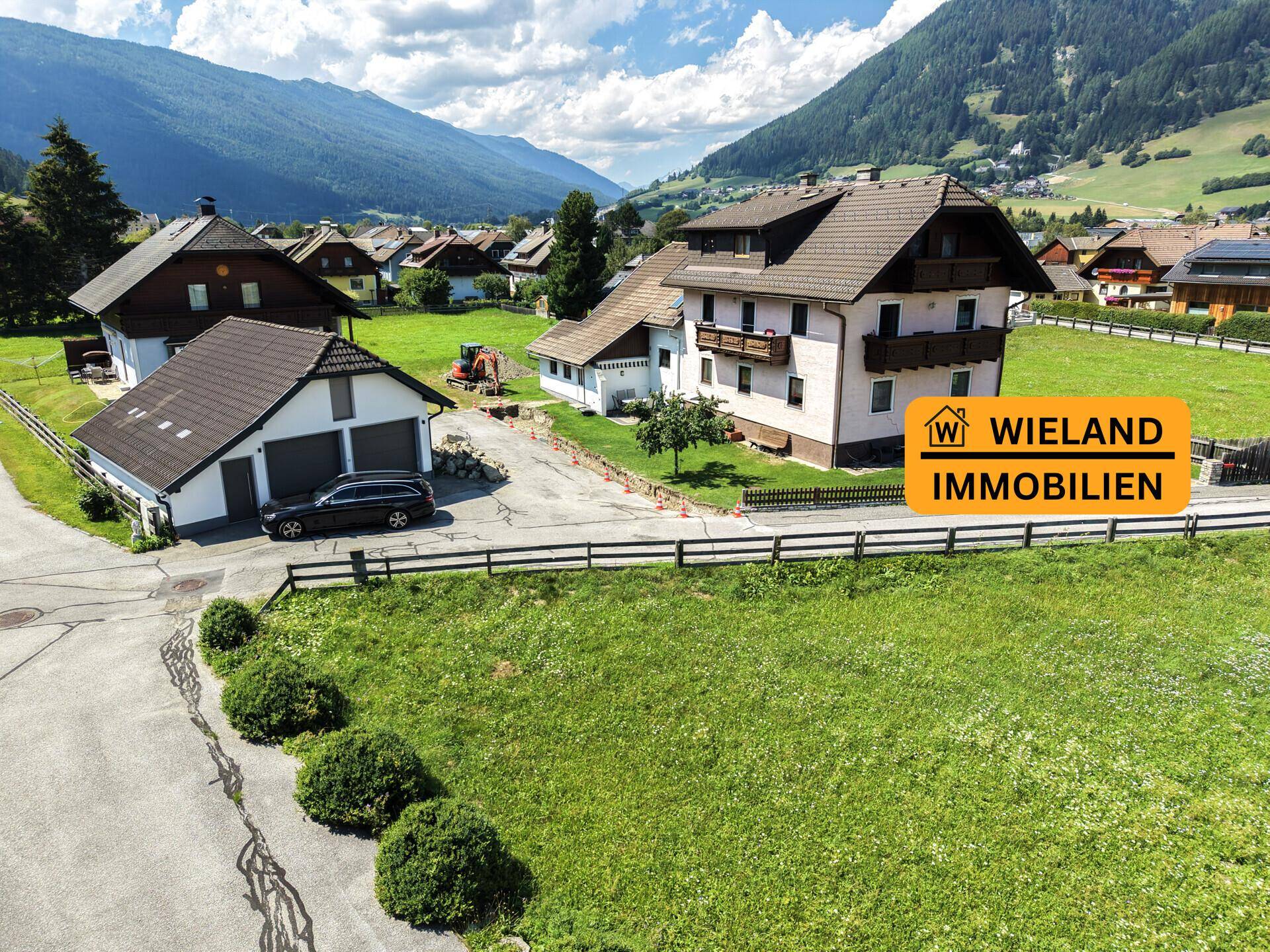 Anwesen mit mehreren Gebäuden, Doppelgarage und weitem Blick auf die umliegende Berglandschaft und grüne Wiesen.