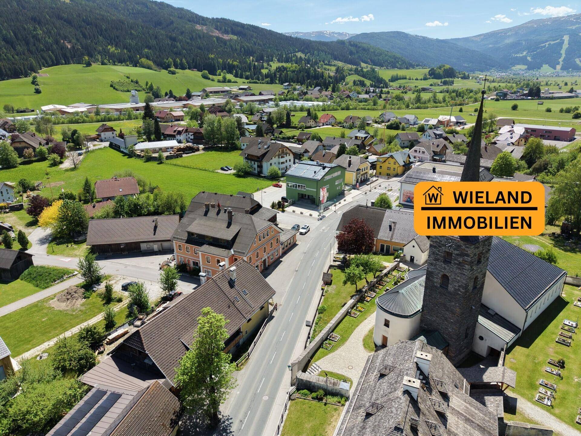 Luftaufnahme des Dorfes Unternberg mit Kirche, Häusern, grünen Feldern und umliegenden Bergen.