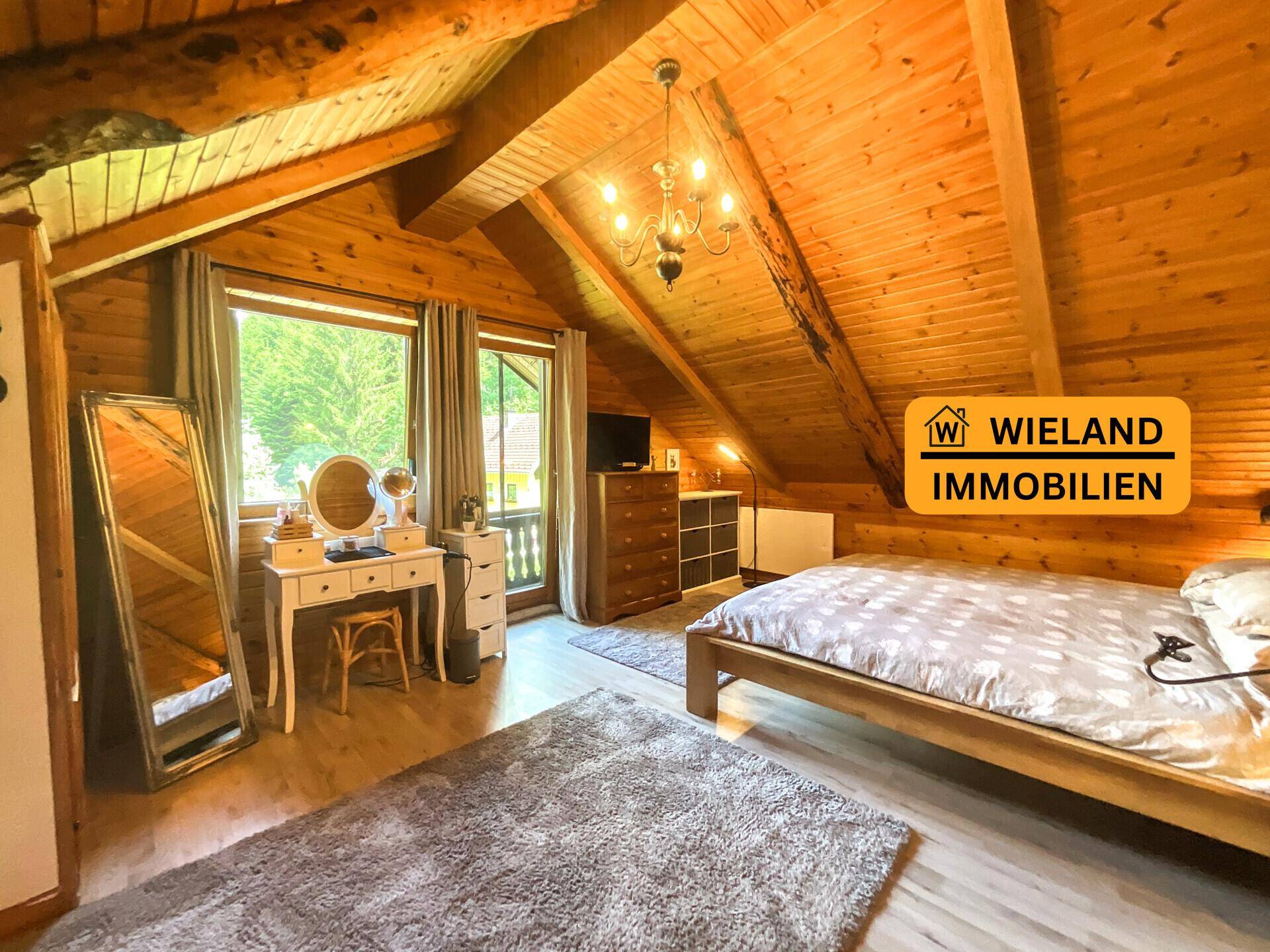 Helles Schlafzimmer mit Holzwänden, Dachschräge und Fensterblick ins Grüne, inklusive Schminktisch.