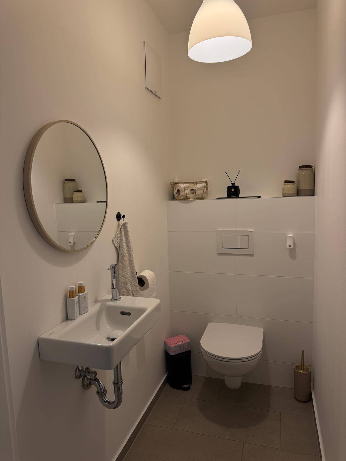 Kleines Gäste-WC mit wandhängendem WC, Waschbecken und rundem Spiegel.