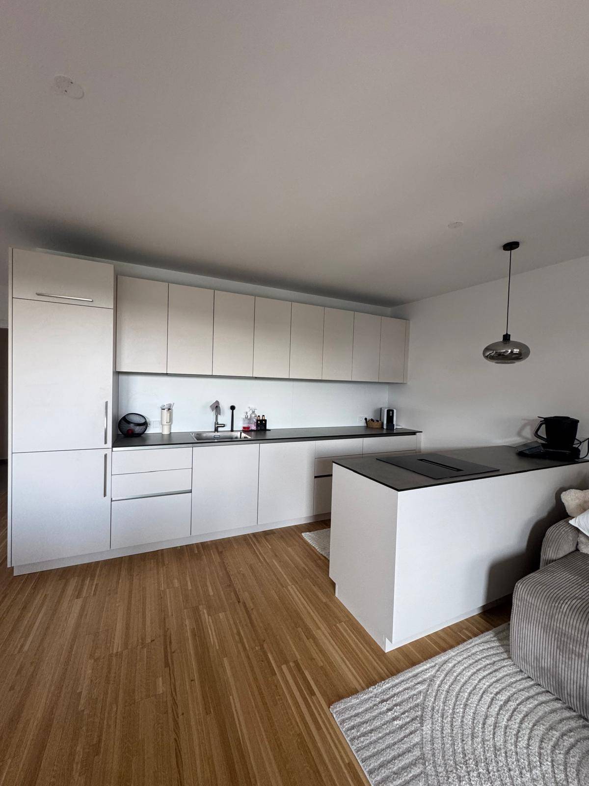 Moderne Einbauküche mit hellen Schränken, dunkler Arbeitsplatte und Holzboden.