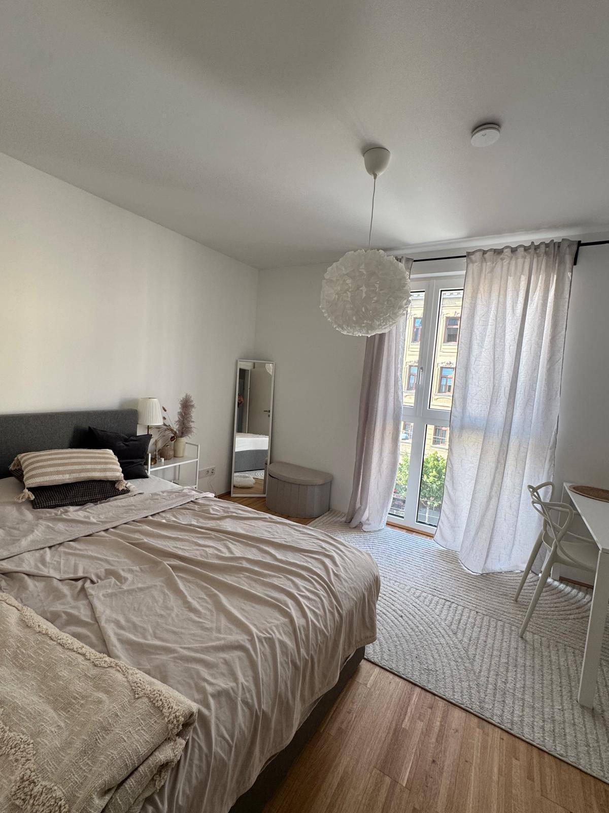 Helles Schlafzimmer mit Doppelbett, Holzboden und Zugang zu einem französischen Balkon.