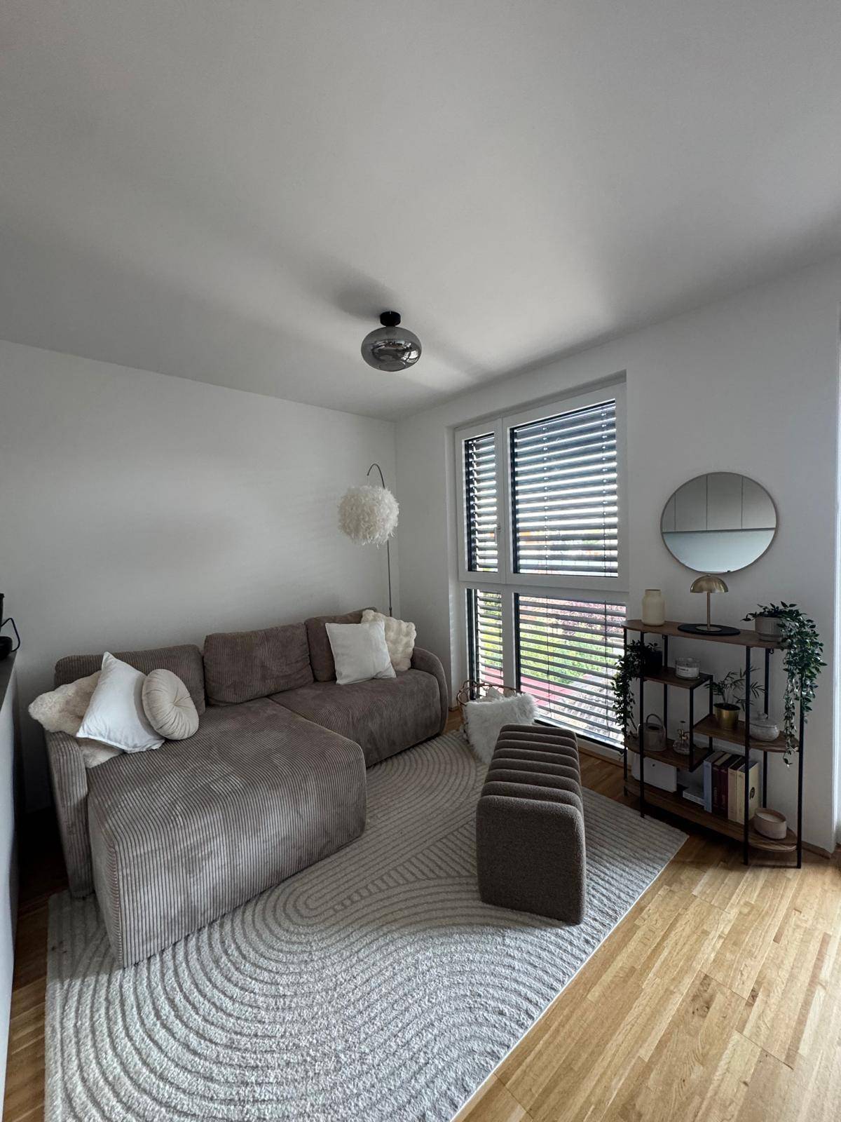 Gemütliches Wohnzimmer mit modernem Sofa, Teppich und großen Fenstern.