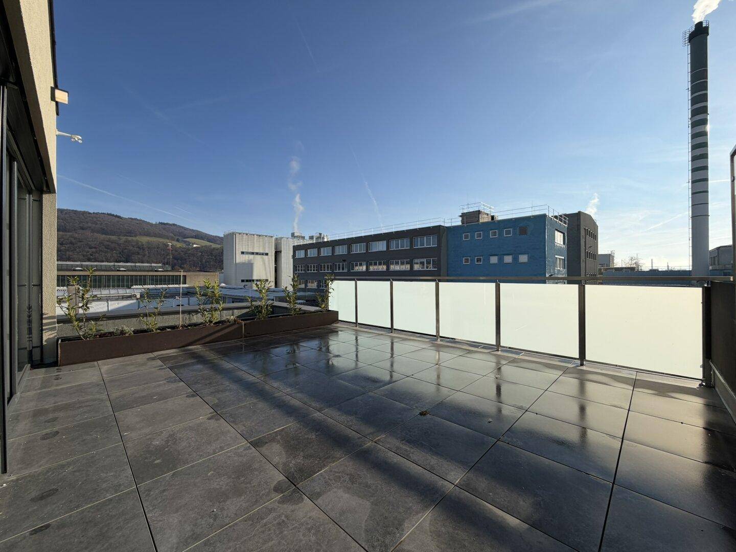 Große, geflieste Dachterrasse mit Blick auf Industriegebäude und die umliegende Landschaft.