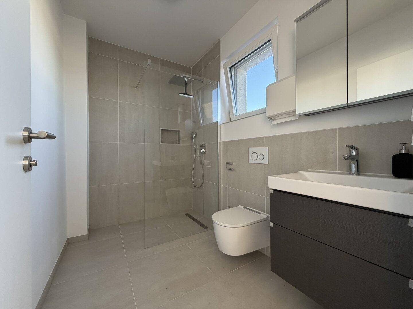 Modernes Badezimmer mit begehbarer Dusche, Hänge-WC und Fenster für Tageslicht.