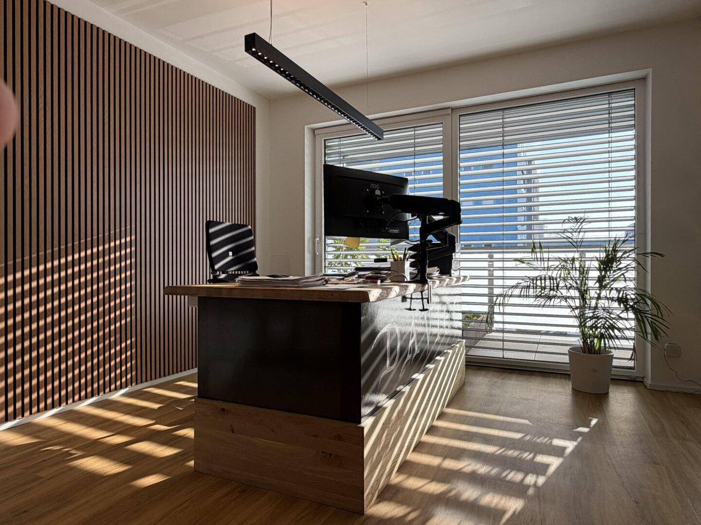 Helles Büro mit Holzwandverkleidung, großem Schreibtisch und Blick nach draußen.